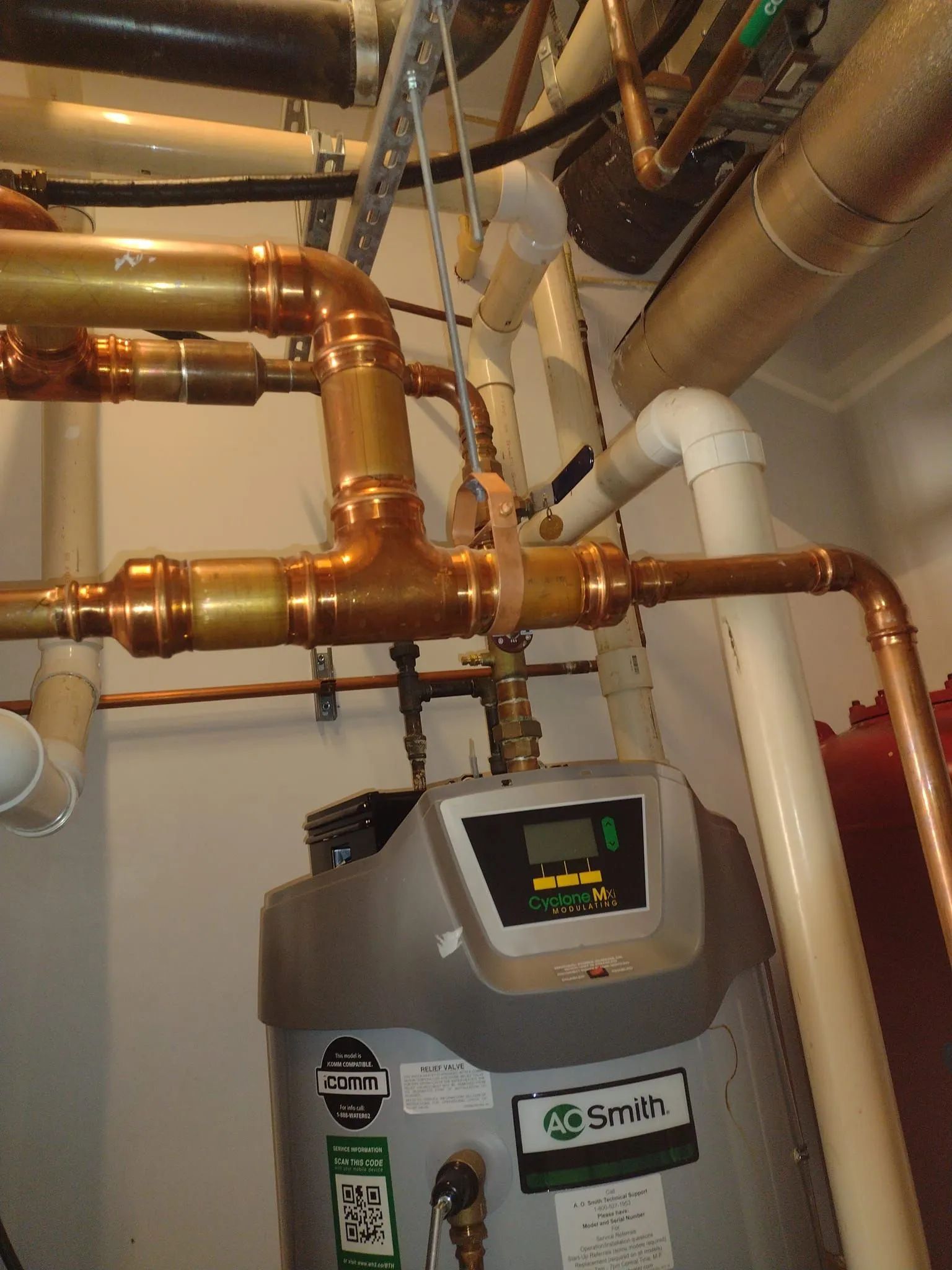 Plumbing pipes of copper and white PVC, connected to an A.O. Smith water heater in a utility room.