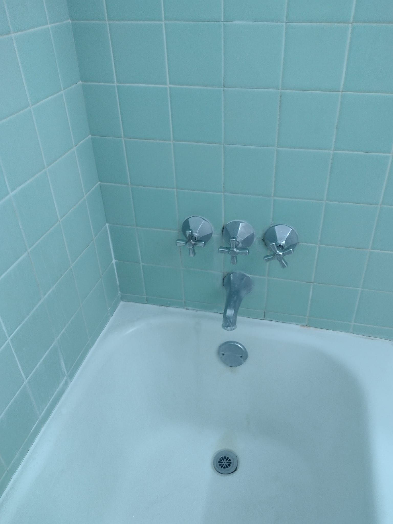A bathtub in a bathroom with green tiles and chrome faucets.
