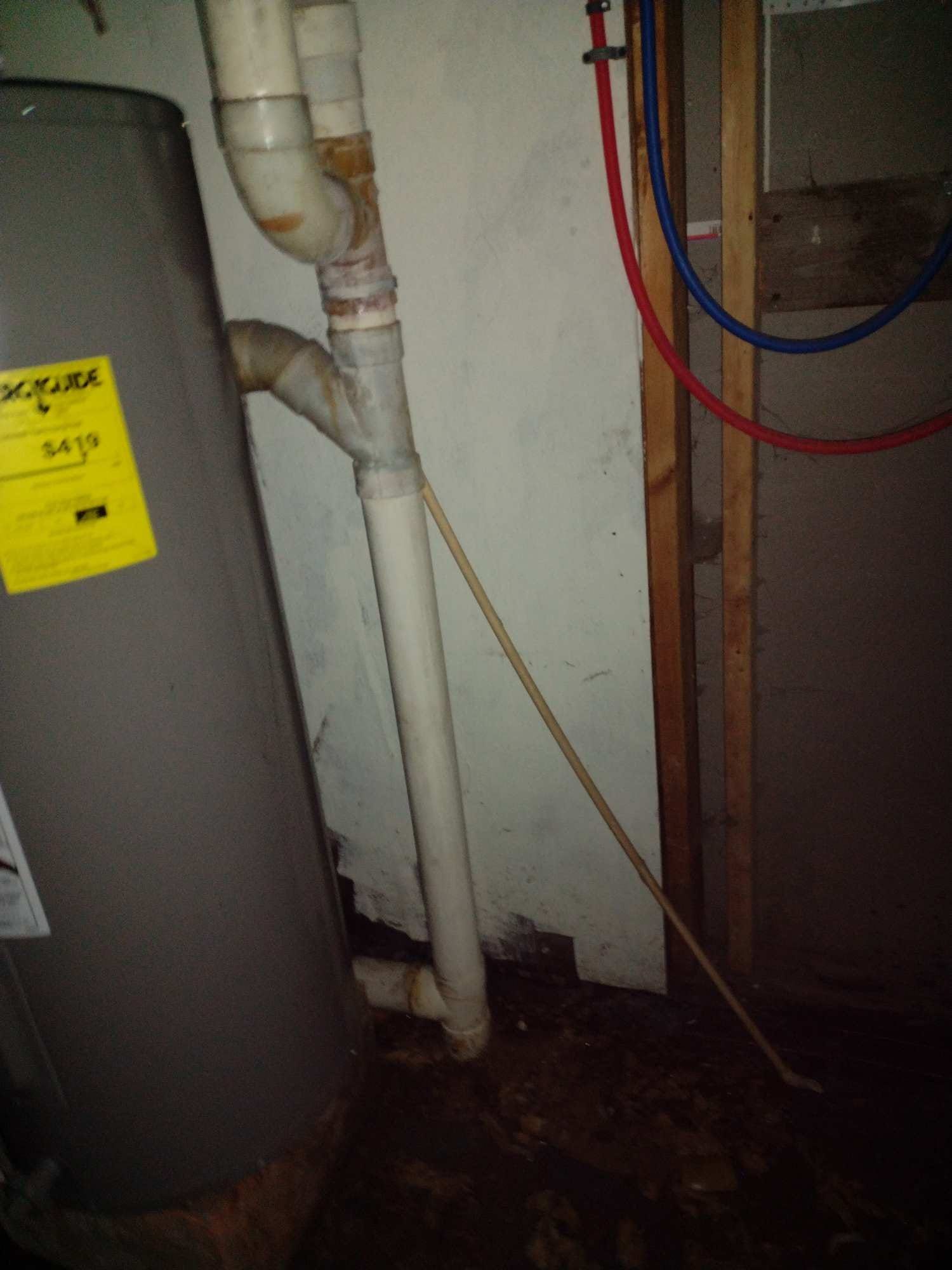 A water heater is sitting next to a pipe in a basement.