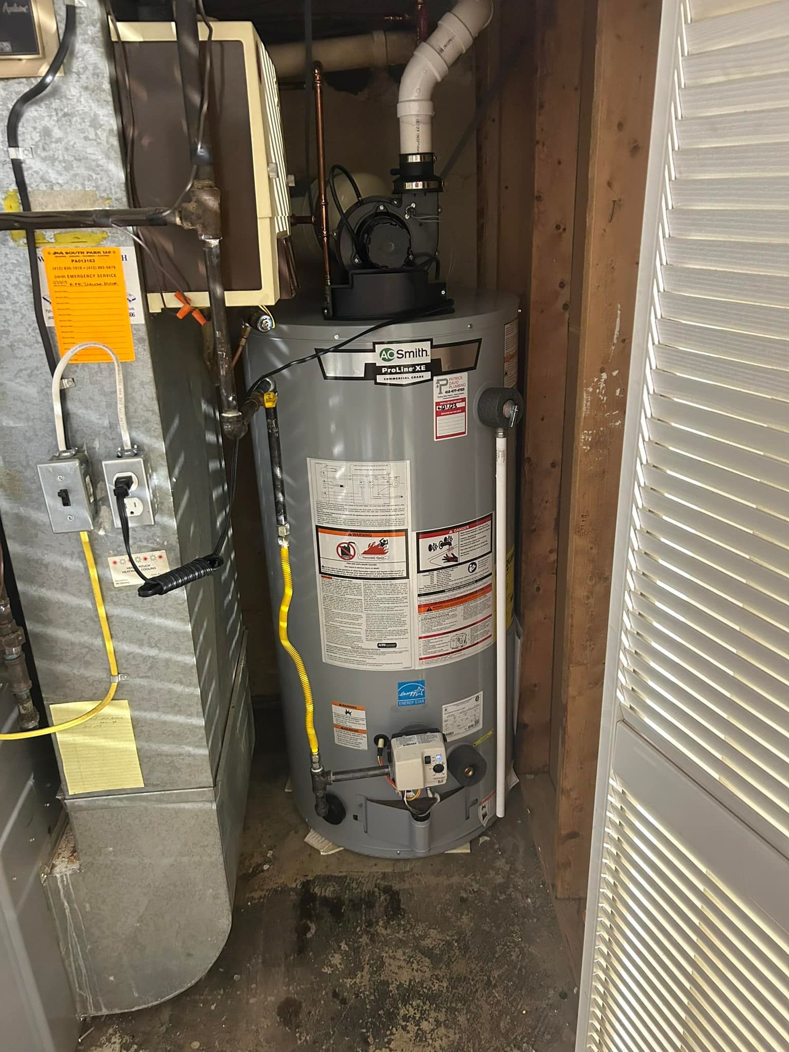 A water heater is sitting in a corner of a room next to a furnace.
