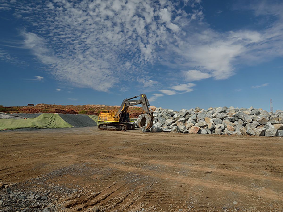 A yellow excavator is sitting in a dirt field next to a pile of rocks.