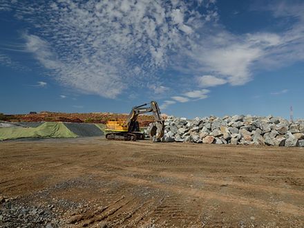 A yellow excavator is sitting in a dirt field next to a pile of rocks.