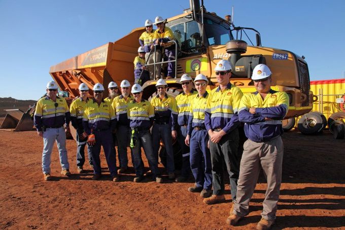 A group of construction workers standing in front of a large yellow truck