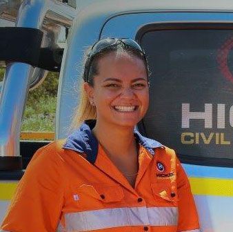 A woman in an orange shirt is smiling in front of a truck.