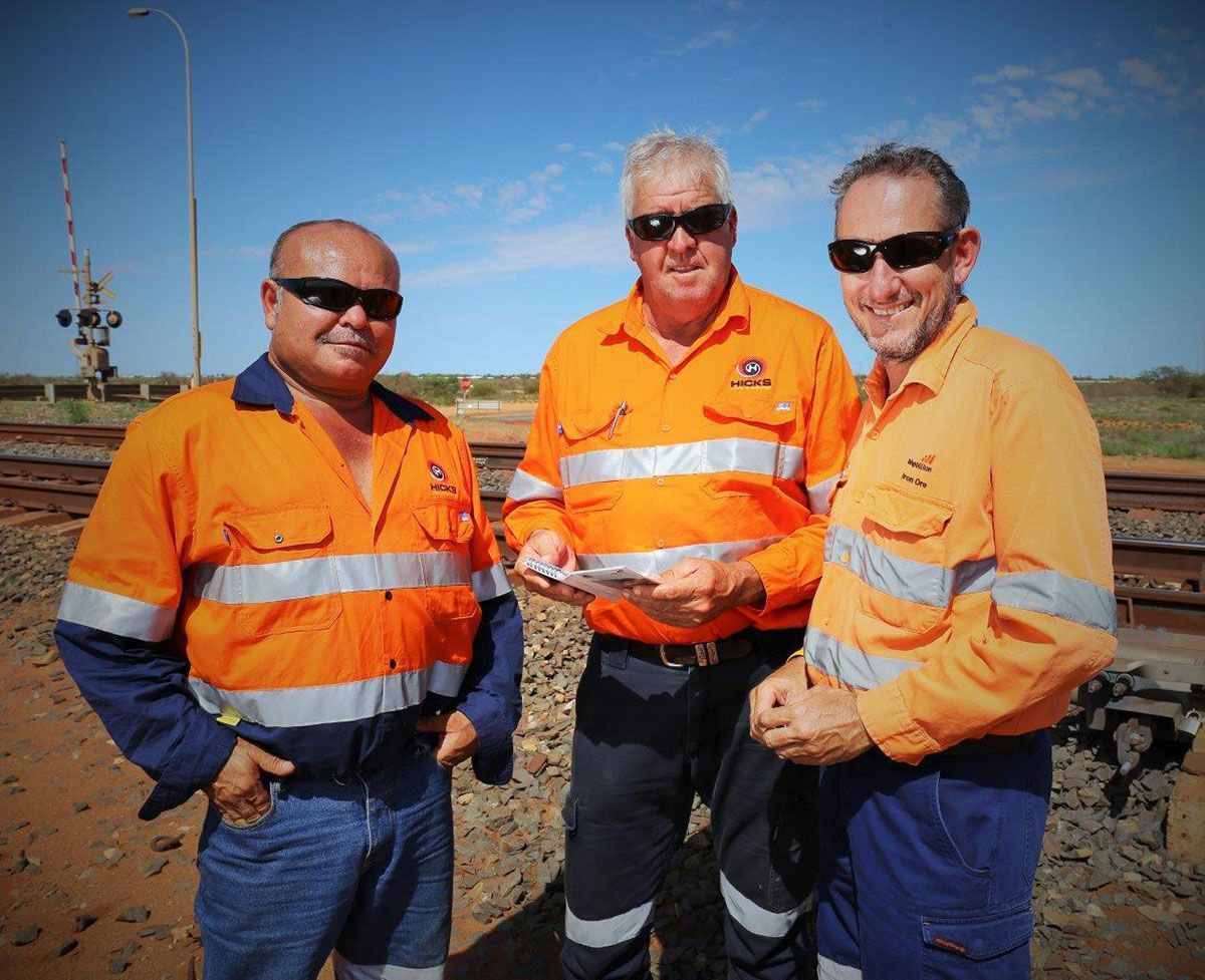 Three men wearing orange safety shirts are standing next to each other