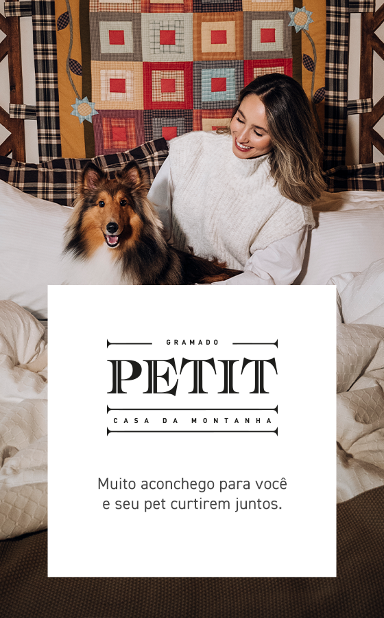 Uma mulher abraça um cachorro em uma cama ao lado de uma placa branca PETIT com a palavra