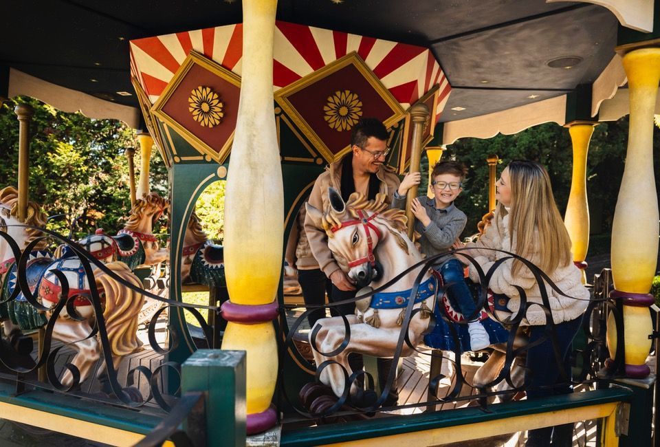 Família passeando em um brinquedo colorido de parque de diversões com toldos listrados e decorações brilhantes.