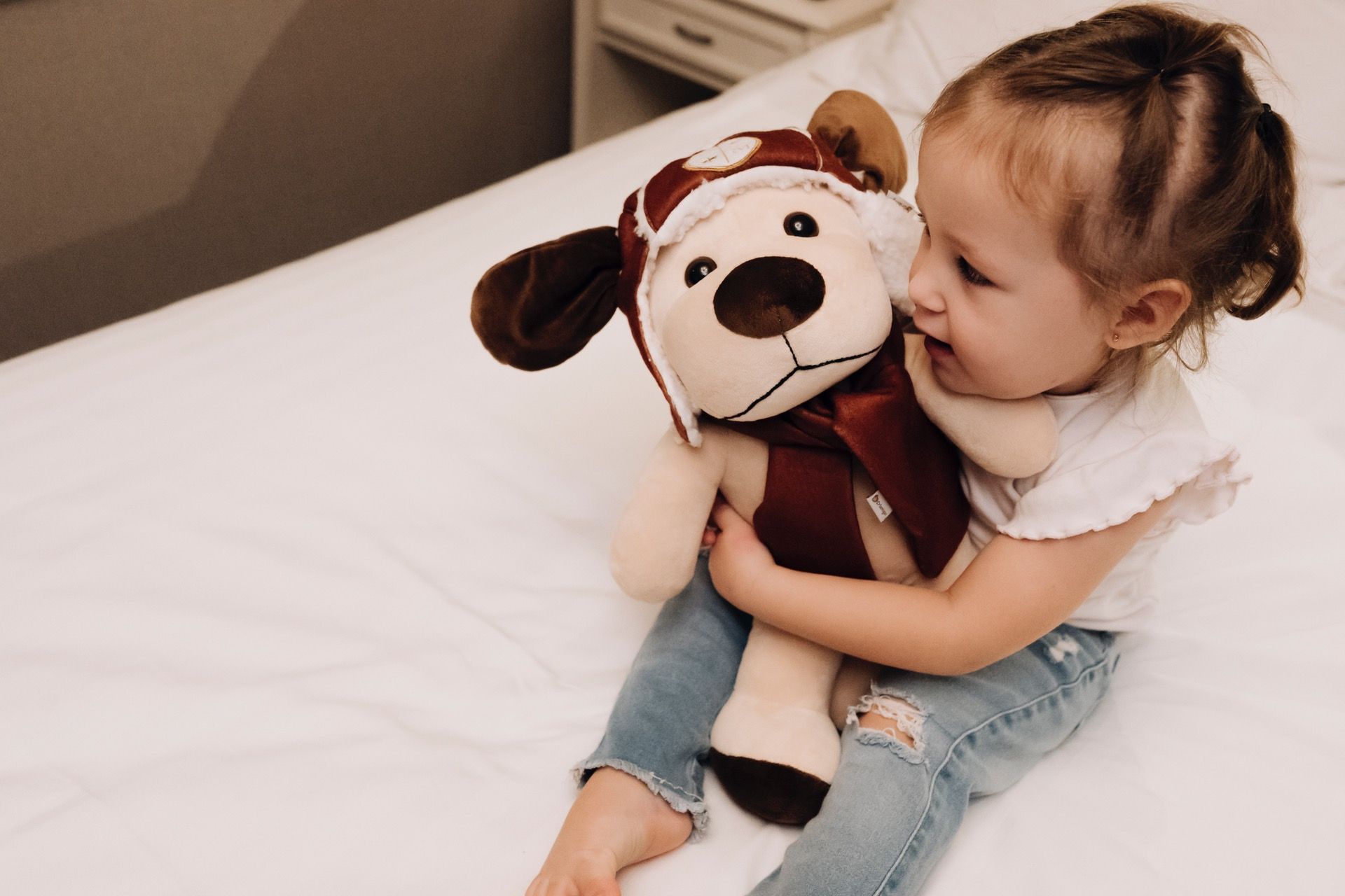 Criança abraçando um cachorro de pelúcia marrom e branco em uma cama.