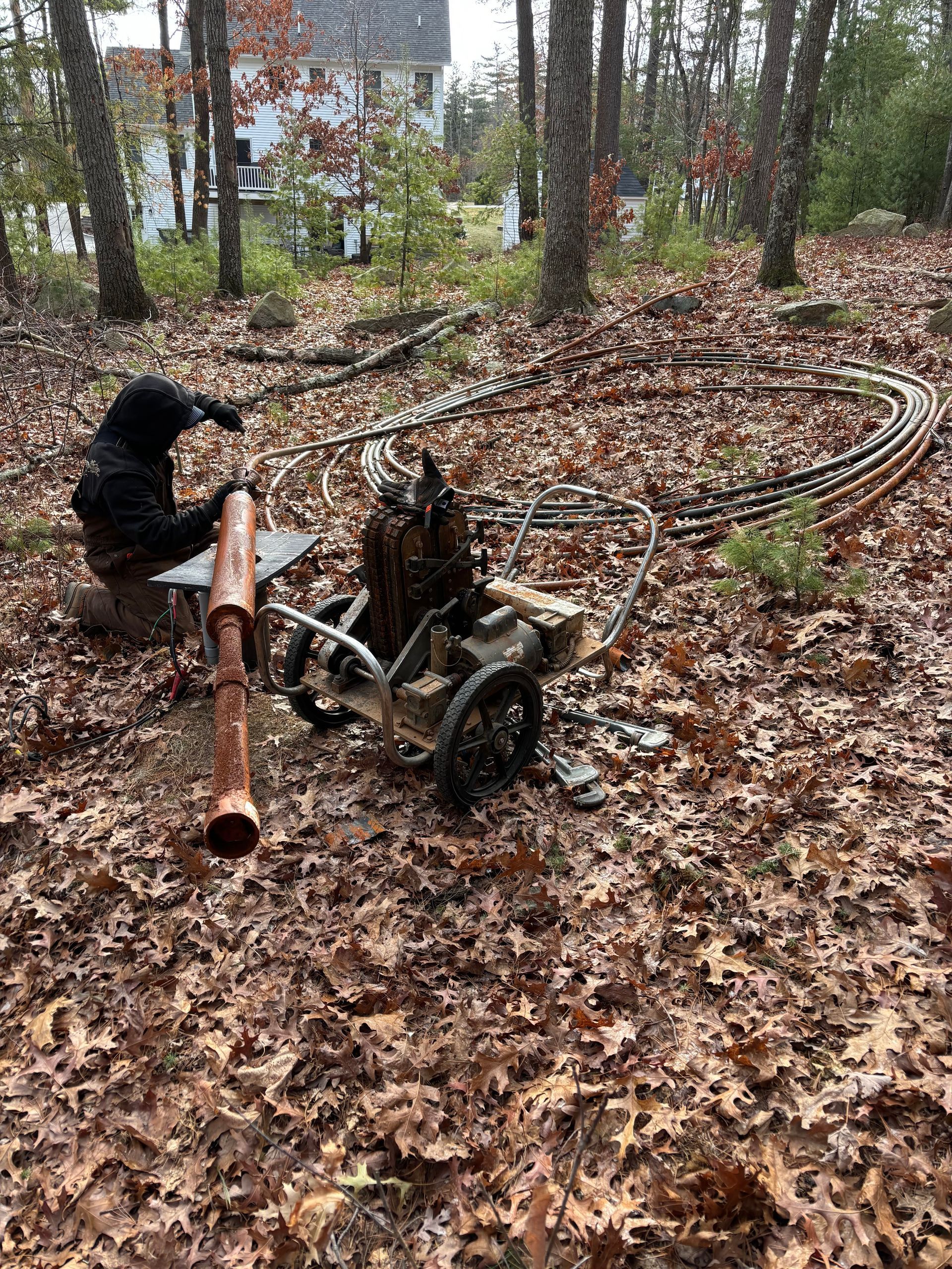 Person operating a homemade cart with pipes in a leaf-covered forest.