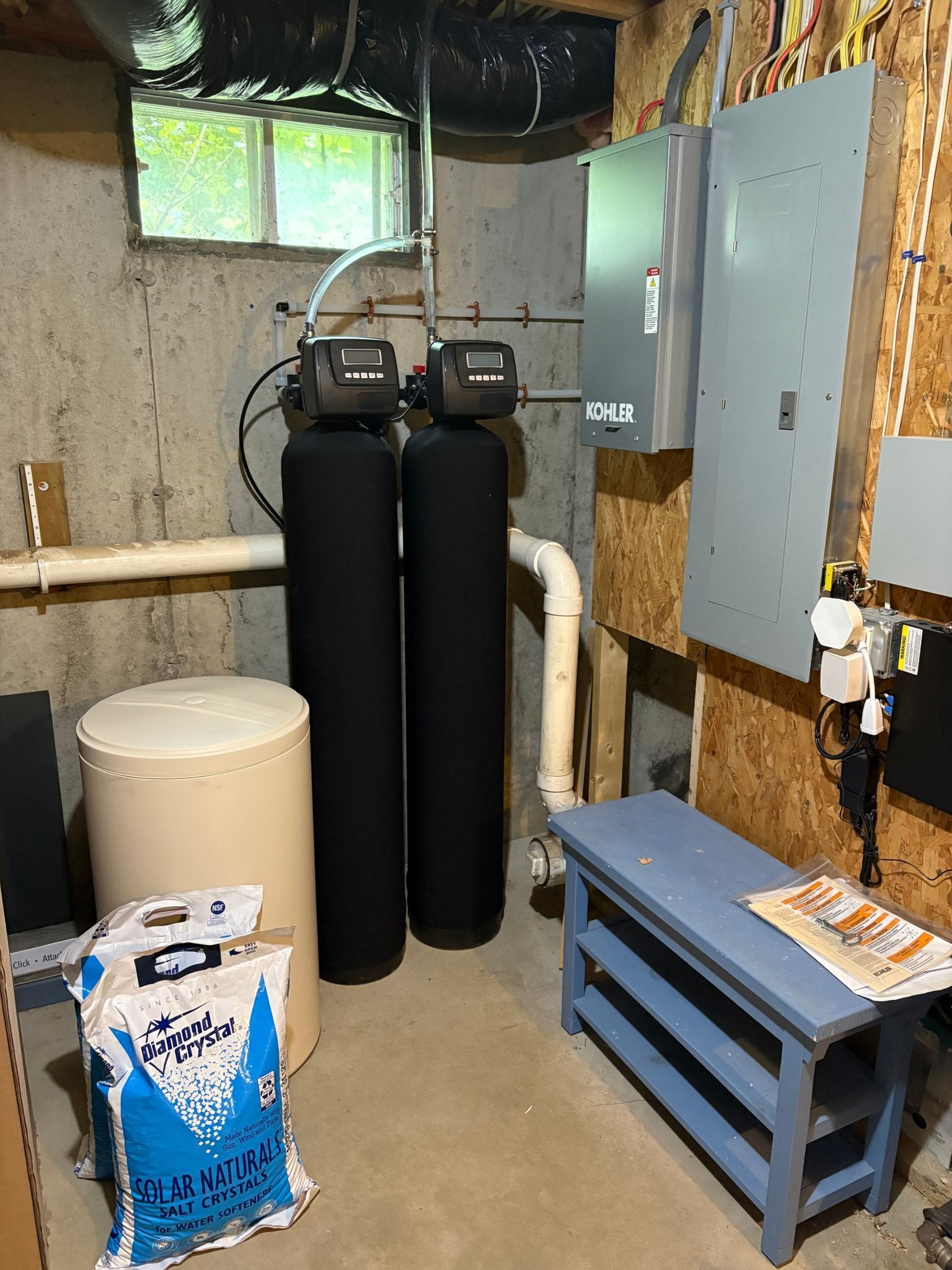 Basement water treatment system with tanks, a panel, and a bench.
