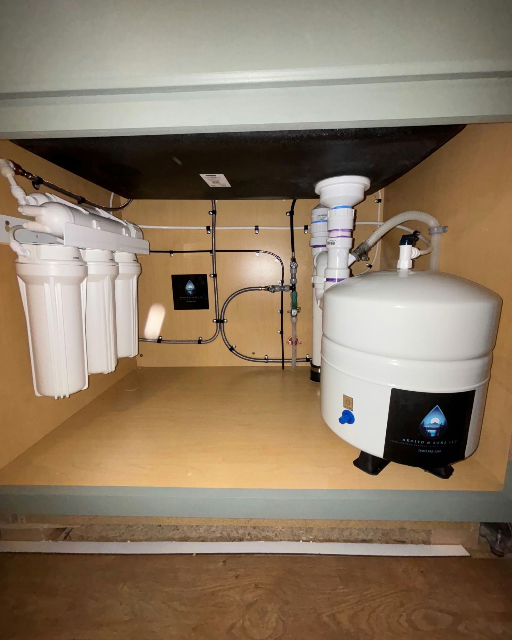 Water filtration system installed in a cabinet, featuring white tanks, blue accents, and beige surroundings.