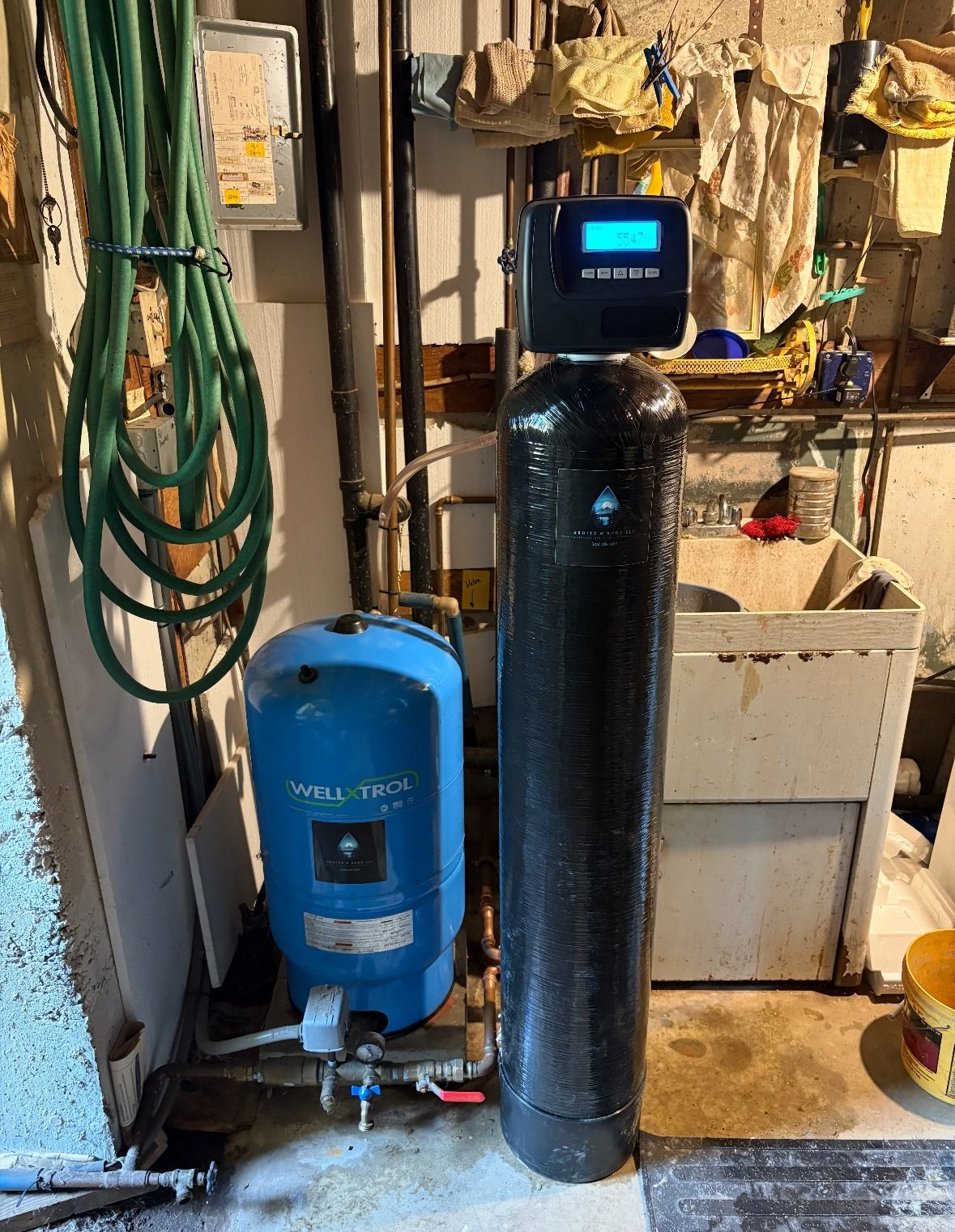 Water softener and pressure tank in a utility room. Black tank with blue display and blue pressure tank.