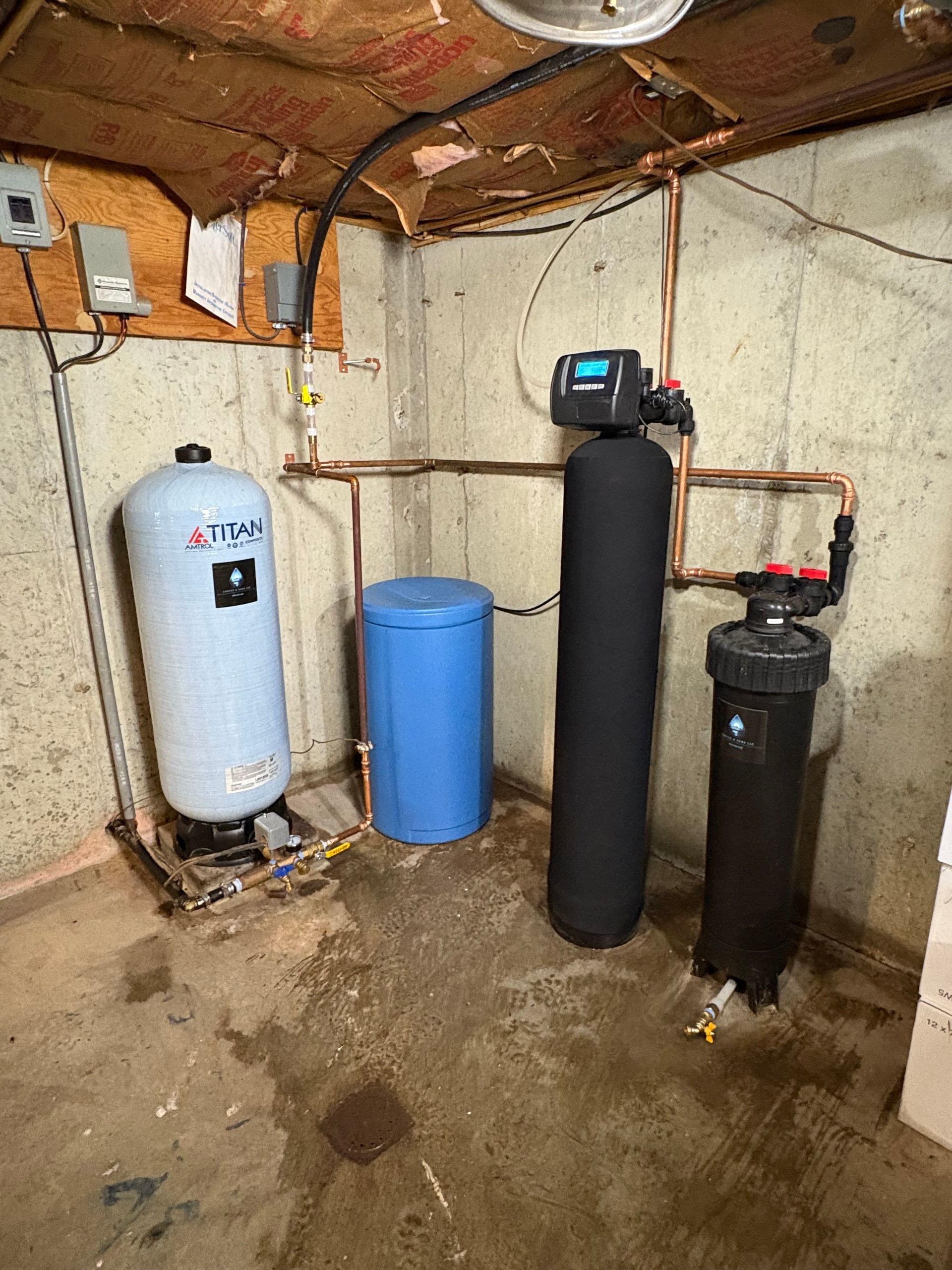 Water treatment system in a basement. Includes a blue water tank, black filter, and pressure tank.