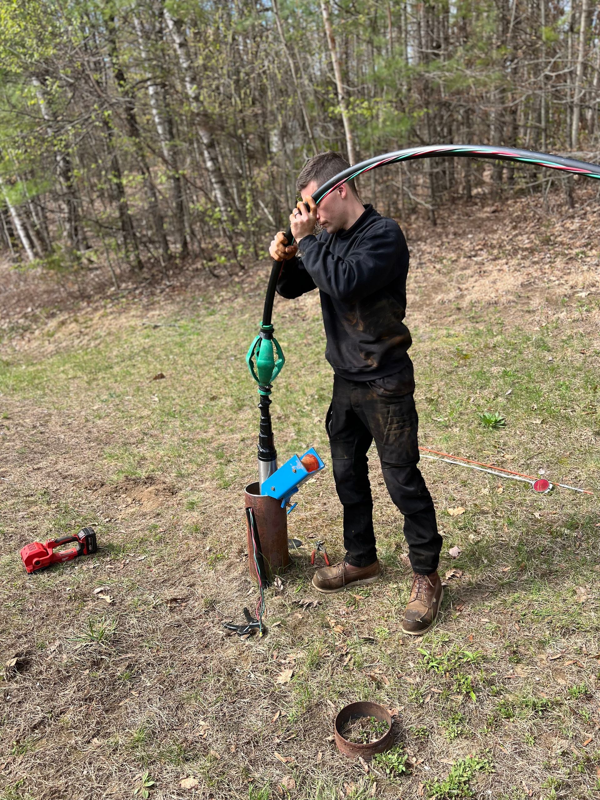 Man in black work clothes uses a pump to extract something from a pipe outdoors.