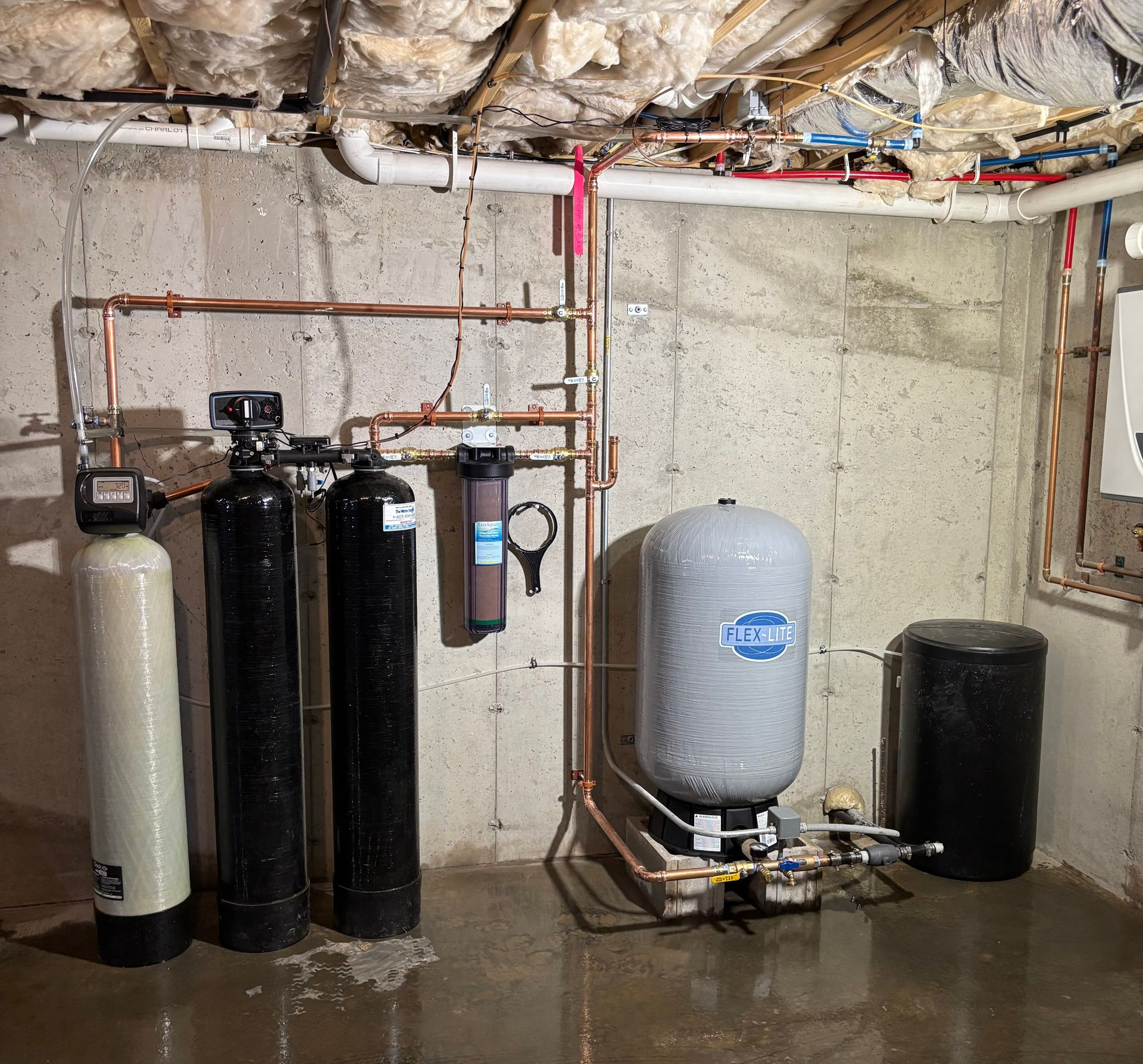 Water treatment system in a basement, including tanks, filters, and pipes.