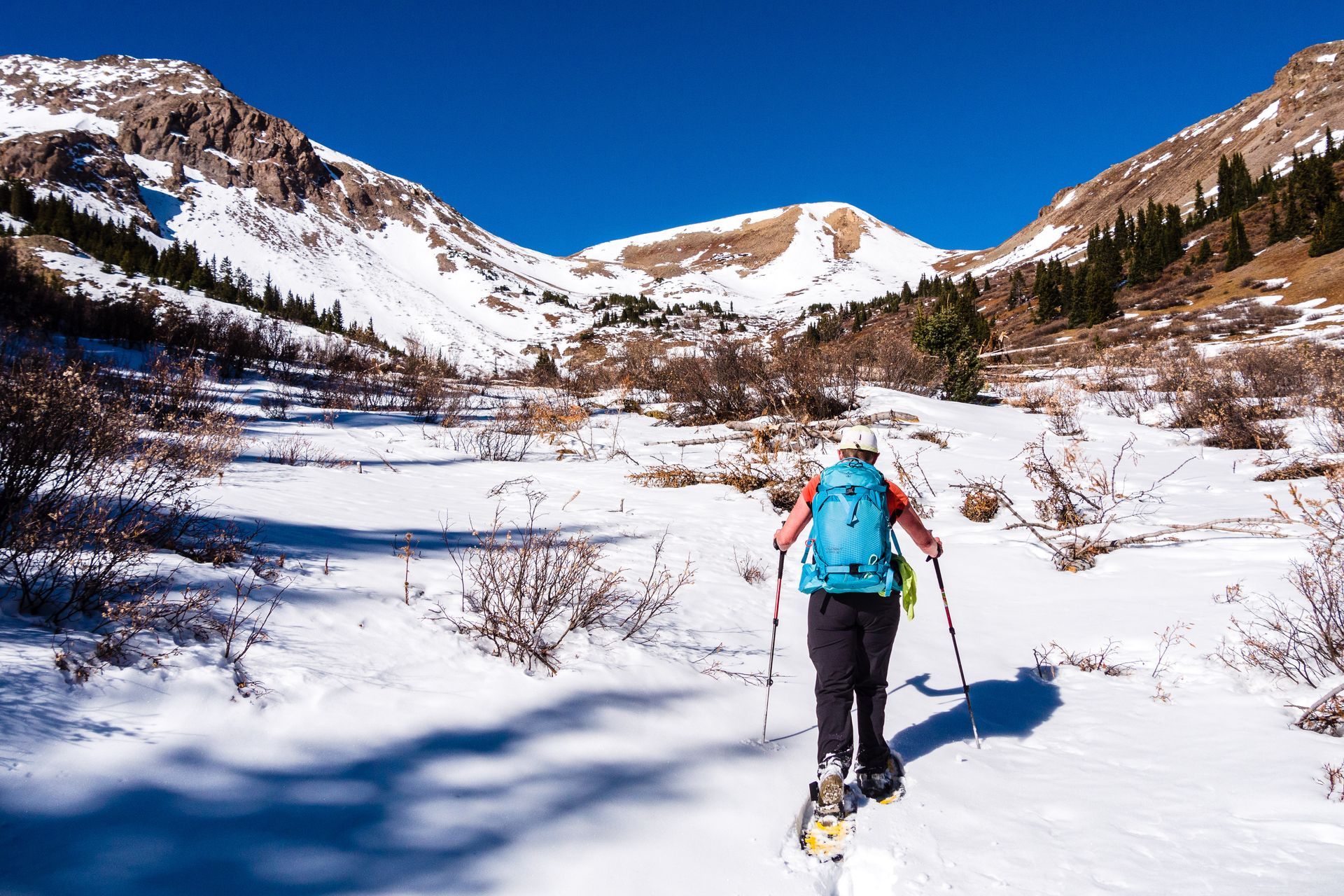 A person is walking through the snow with a backpack and snowshoes.