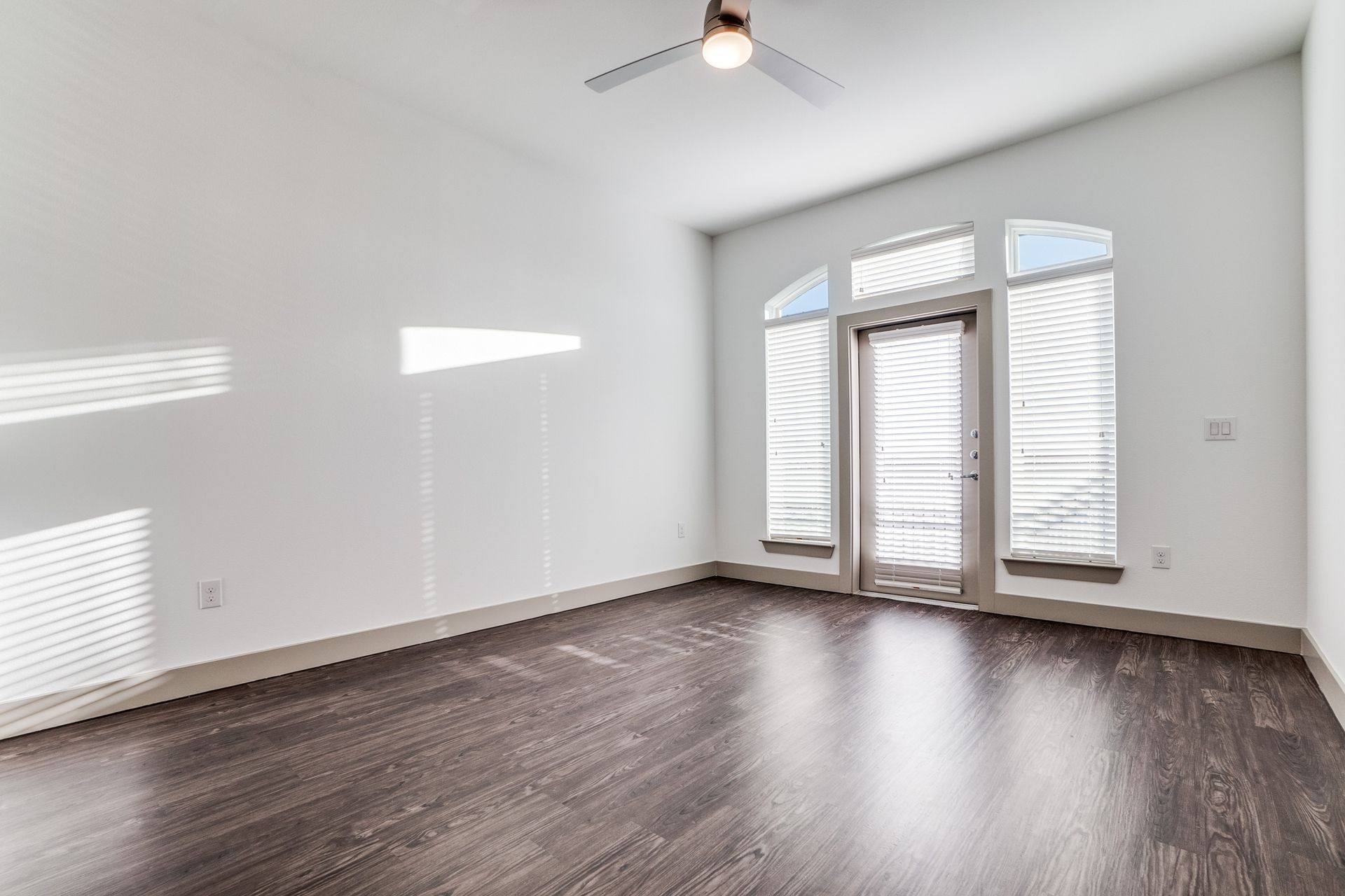 An empty living room with hardwood floors and a ceiling fan.
