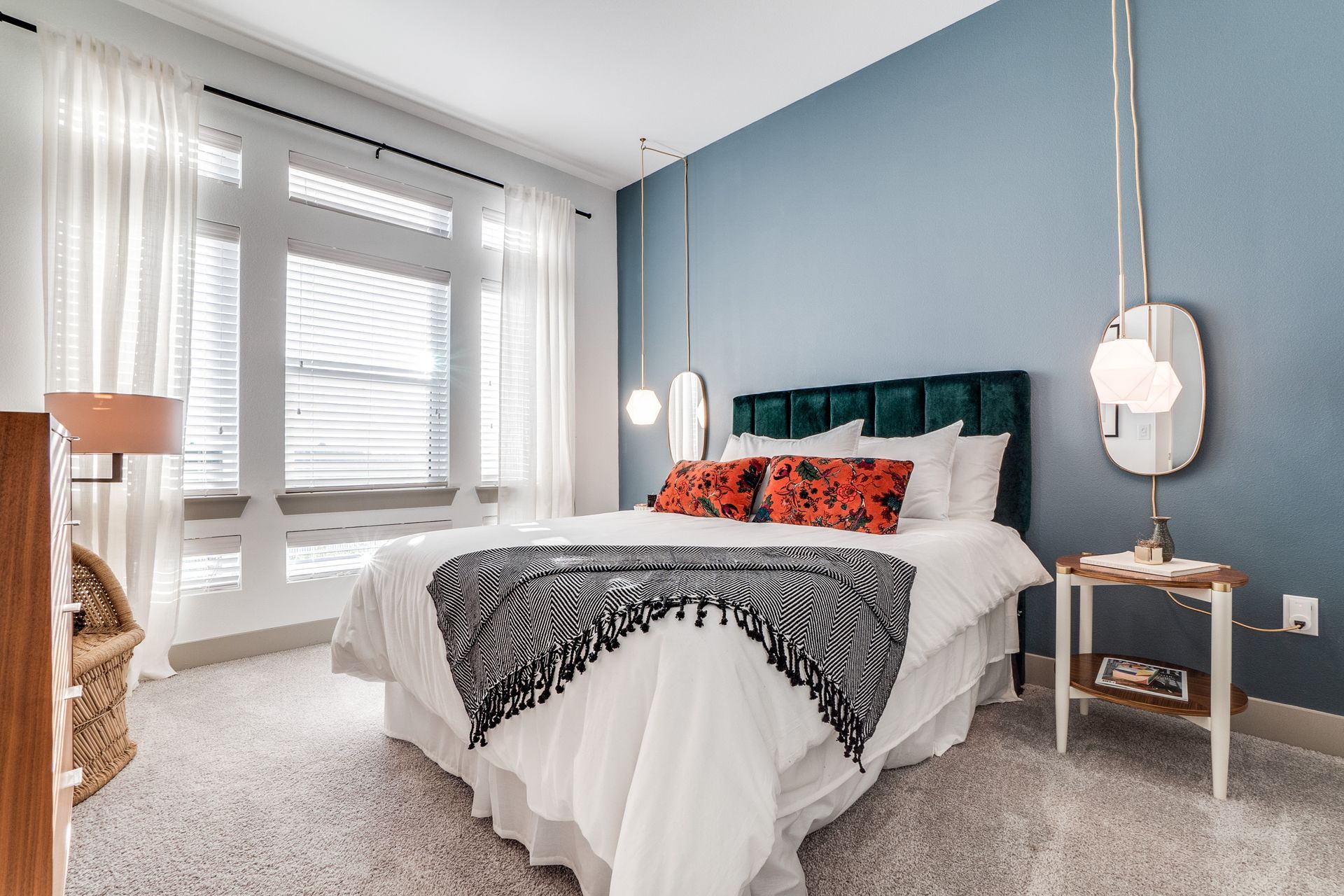 A bedroom with a bed , nightstand , mirror and window.