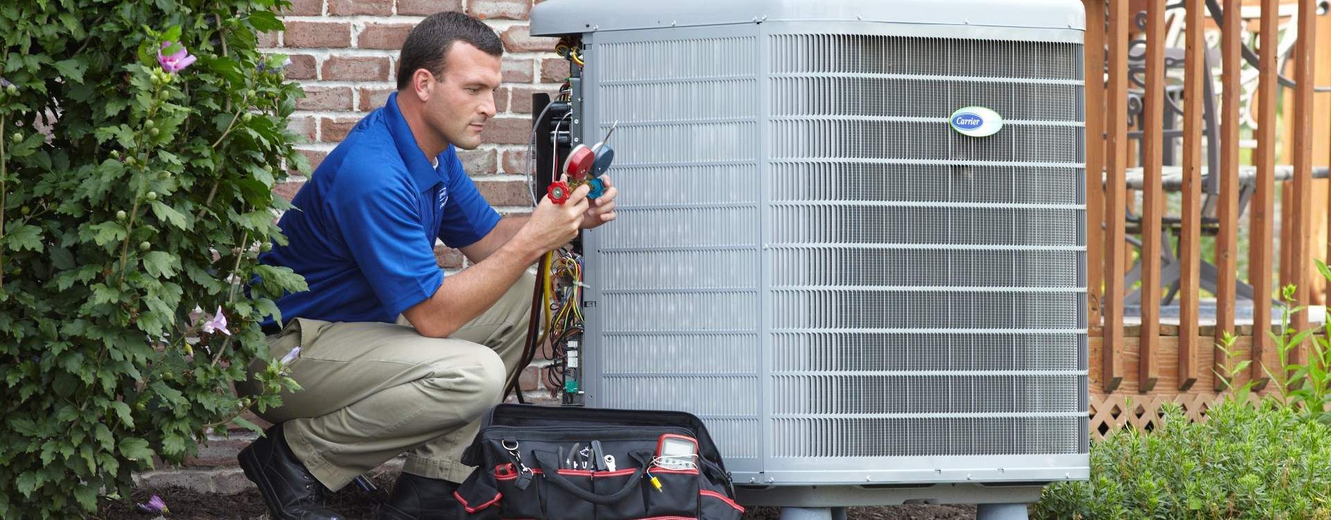 A man is kneeling down in front of an air conditioner.