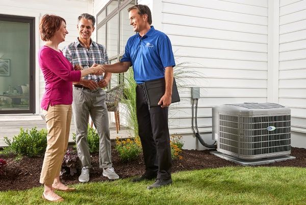 A man and a woman are shaking hands with a man in front of a house.