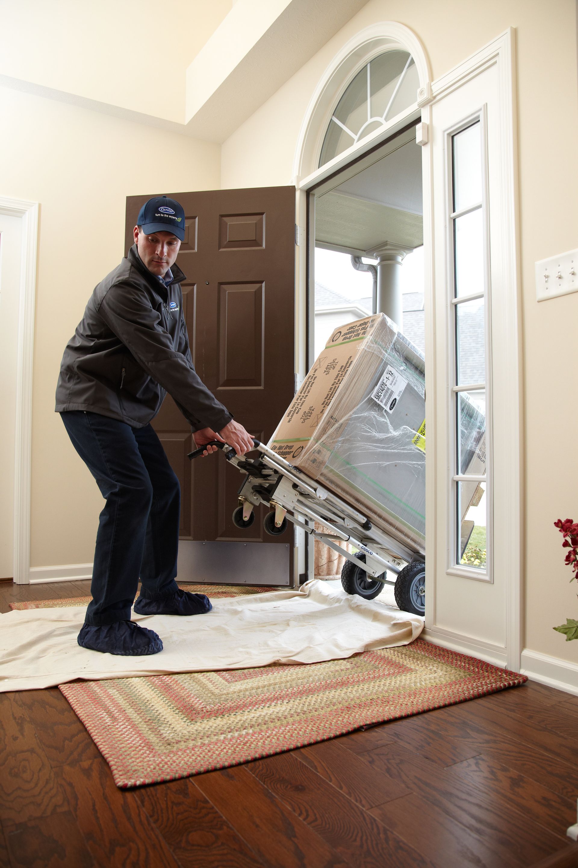 A man is pushing a refrigerator on a dolly into a doorway.