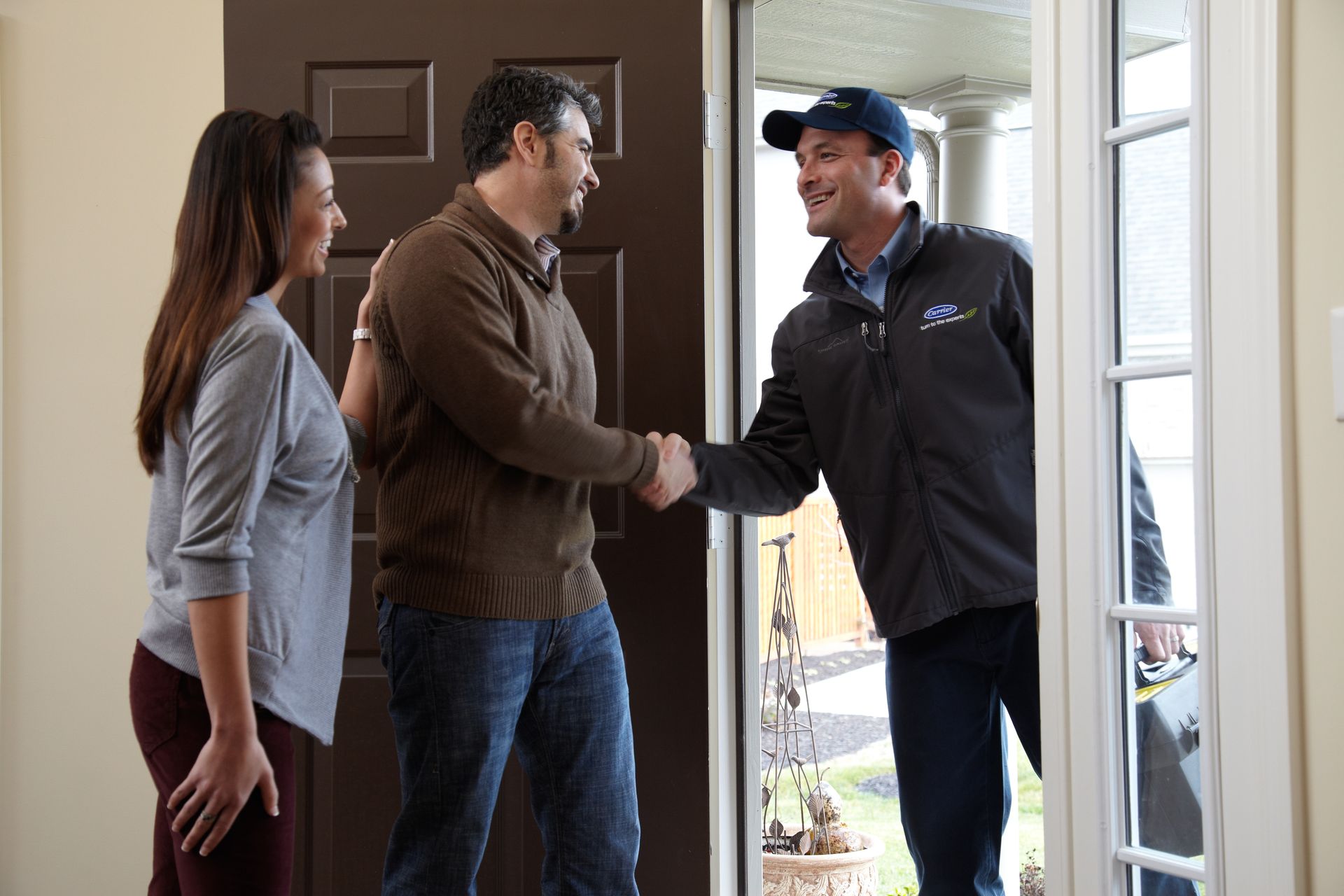 A man and woman are shaking hands with a man in a doorway.