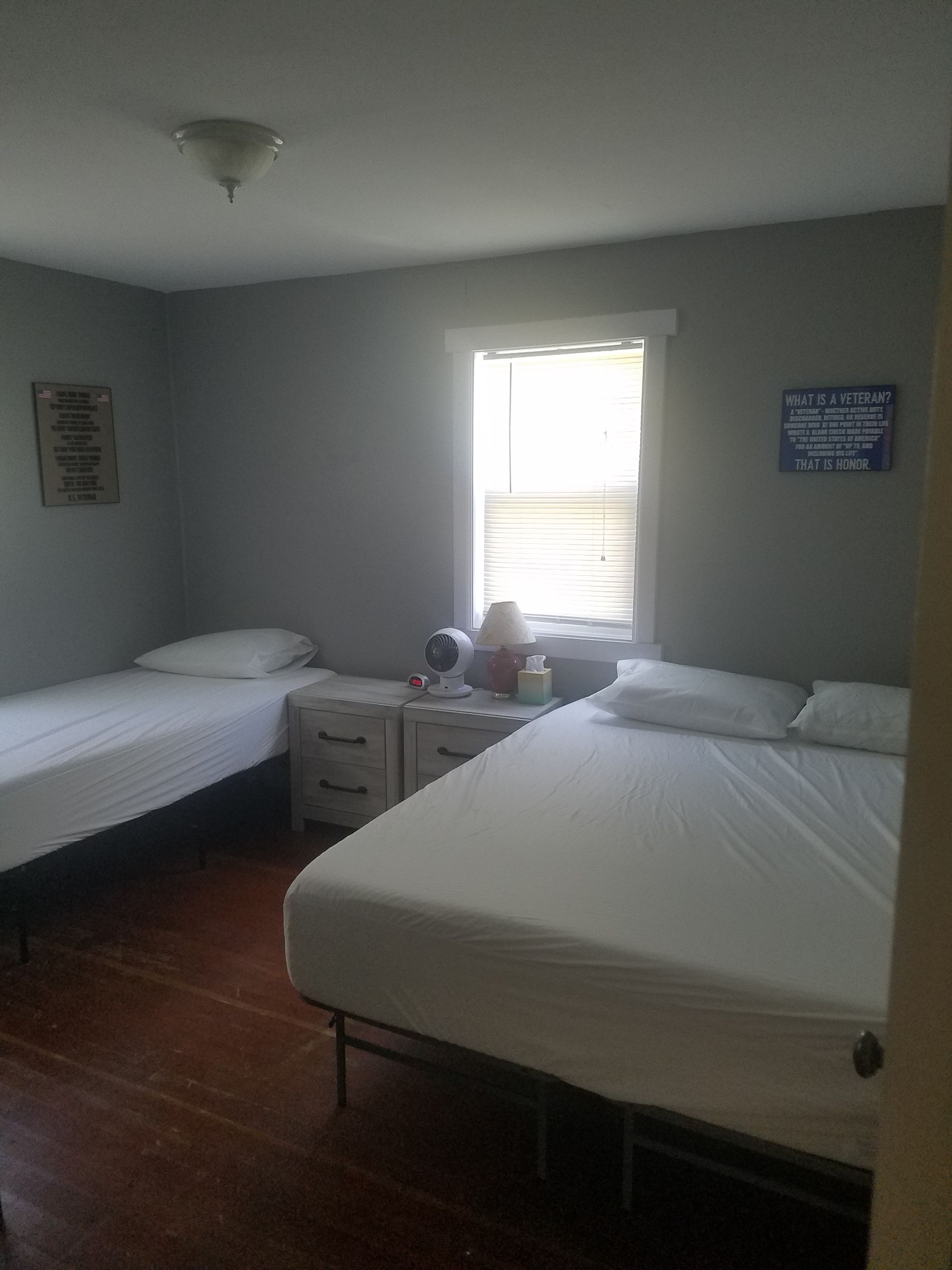 A bedroom with two beds , two nightstands and a window.