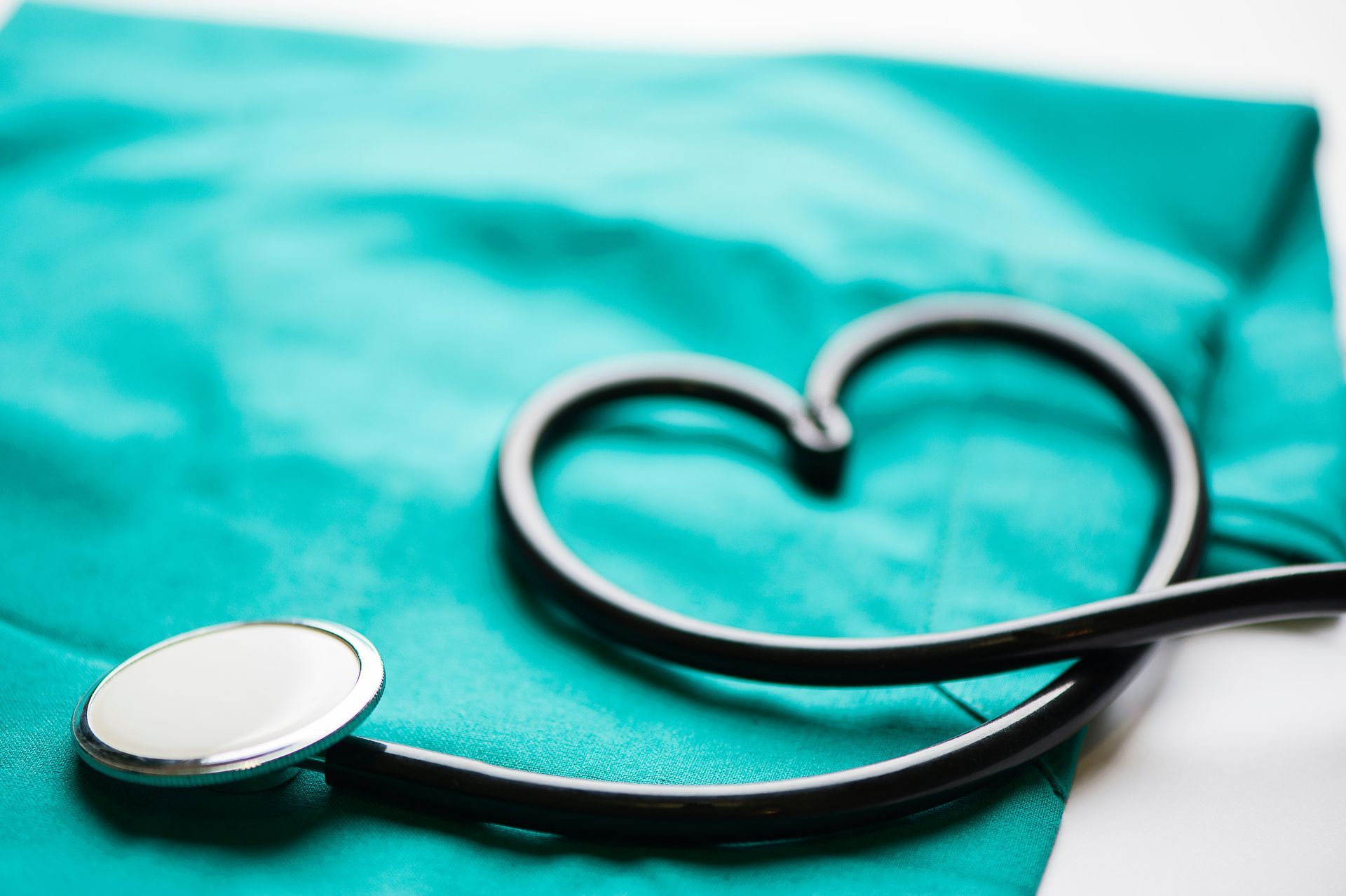 Ein Stethoskop in Herzform liegt auf grünem medizinischen Stoff, symbolisch für die Gesundheitsfürsorge und die Liebe zum medizinischen Beruf. 