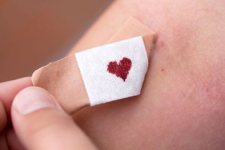 Ein hautfarbenes Pflaster auf einer Person mit einem kleinen, roten Herz in der Mitte, das einen Tupfer Blut darstellt.
