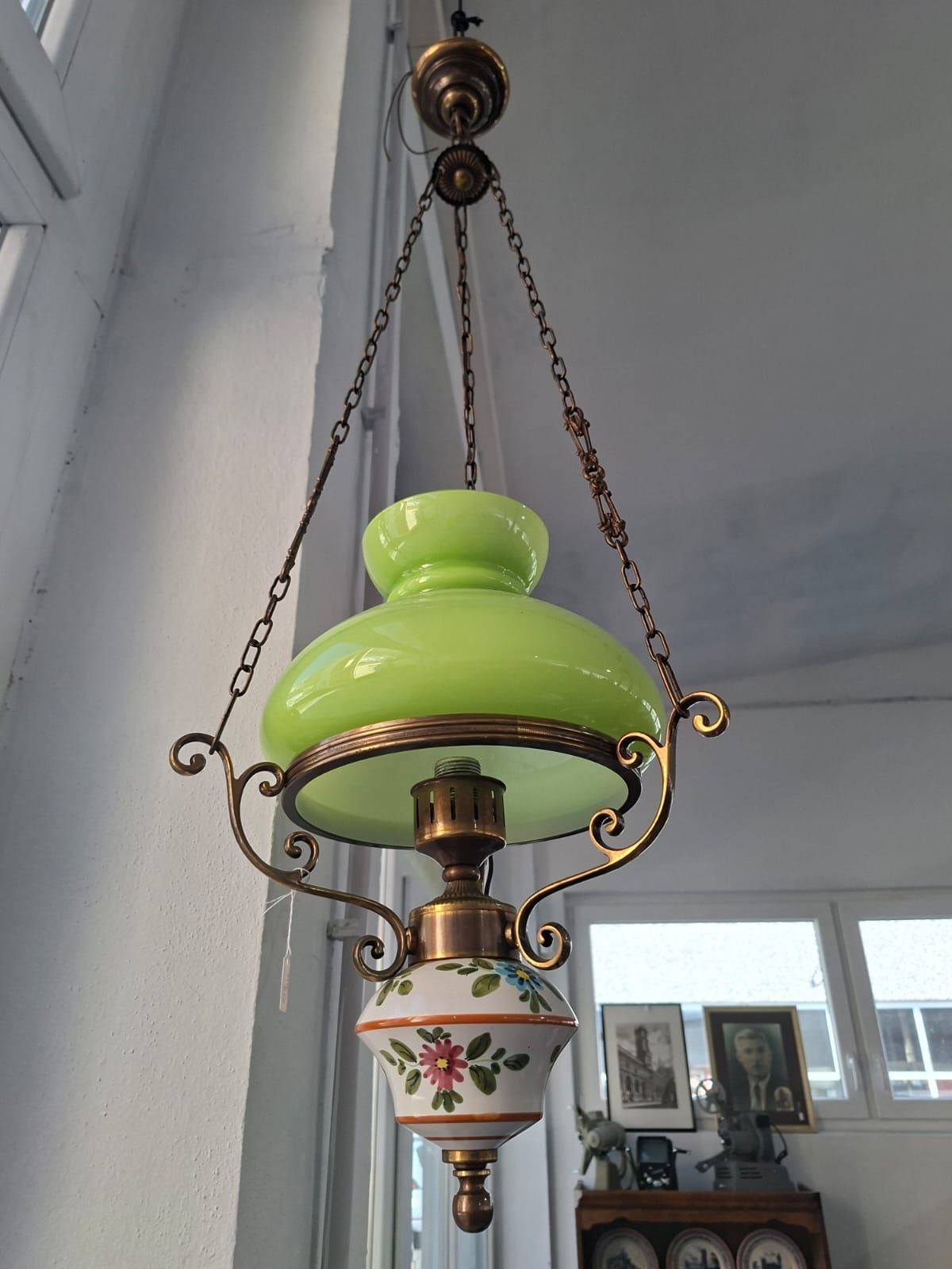 Lampada a sospensione vintage con paralume in vetro verde lime sopra una base in ceramica decorata con motivi floreali, sospesa tramite catene.