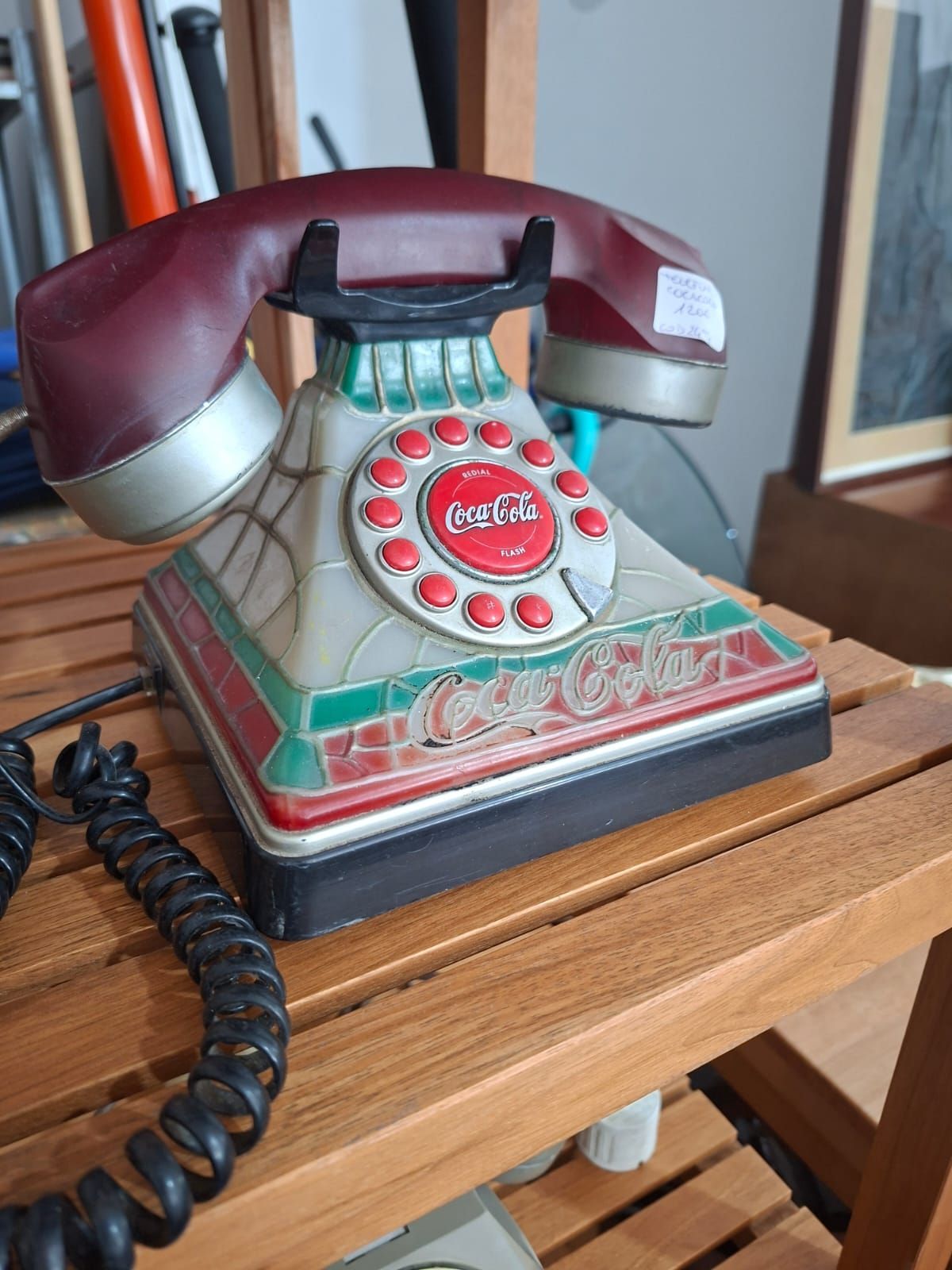Un telefono decorativo a tema Coca-Cola con base in stile vetrata, dettagli rossi e cornetta color bordeaux scuro.
