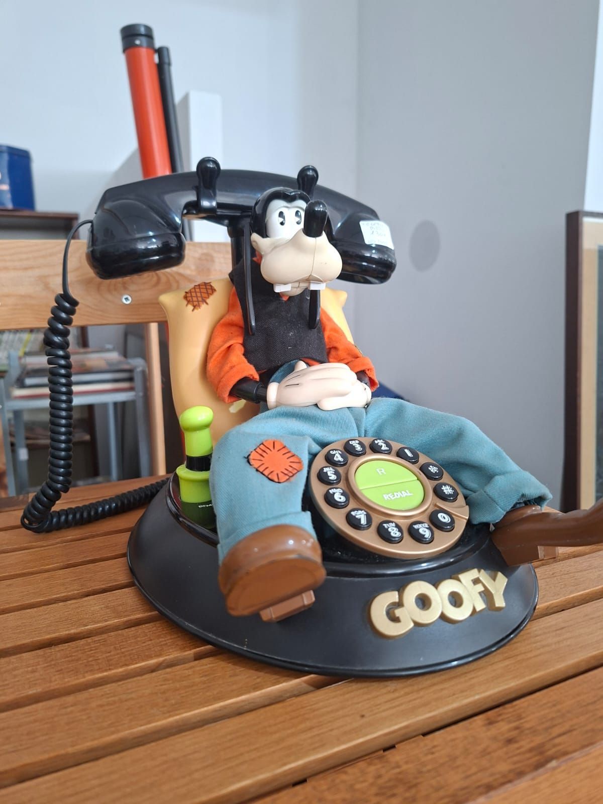 Un telefono da scrivania a tema Pippo, con una statuetta di Pippo seduto che tiene in mano una tastiera a disco, appoggiata su un tavolo di legno.
