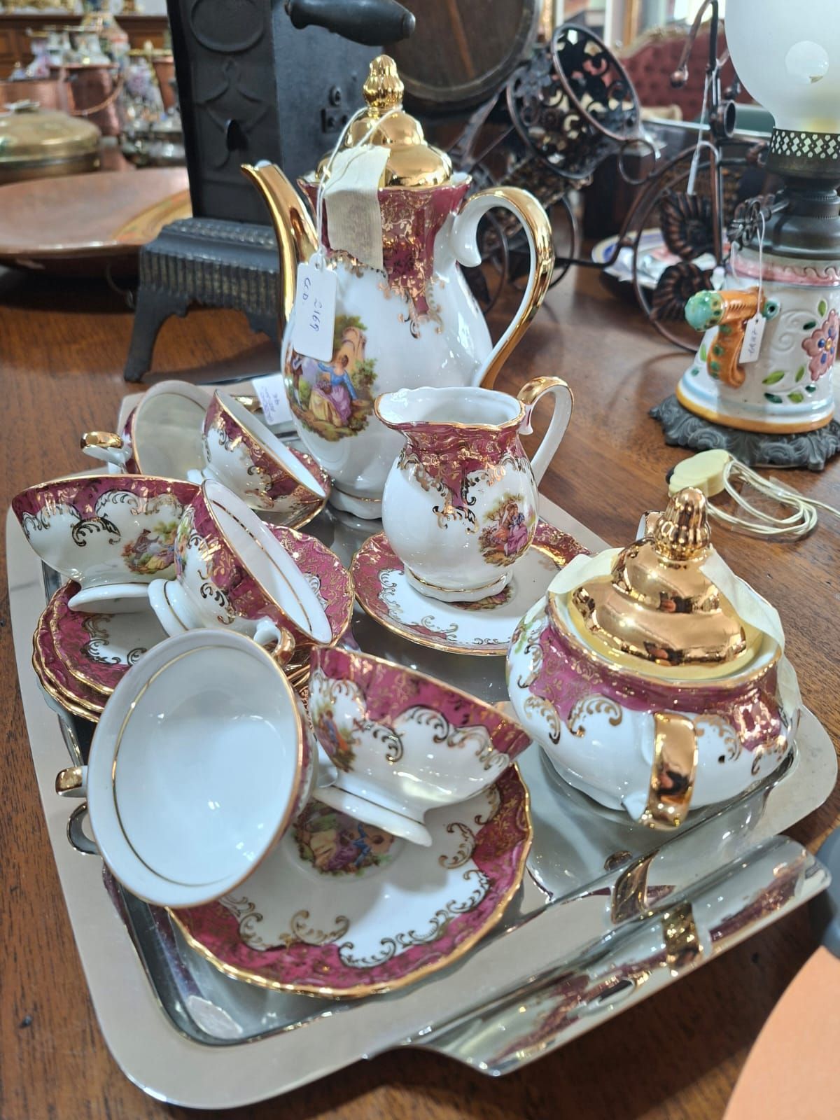 Un servizio da tè vintage in porcellana con decorazioni floreali bianche, dorate e rosse è appoggiato su un vassoio d'argento sopra un tavolo di legno.