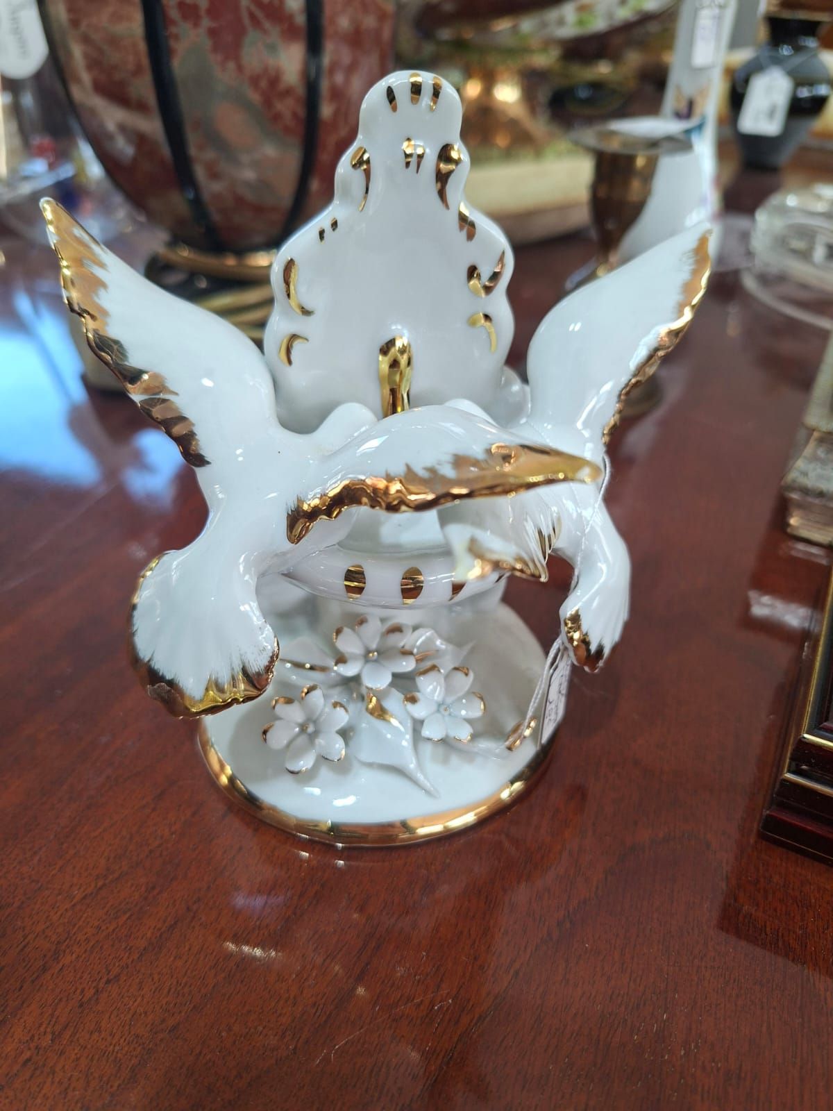 Una statuetta in porcellana bianca con bordi dorati raffigurante due uccelli con le ali spiegate sopra una base decorata con fiori.