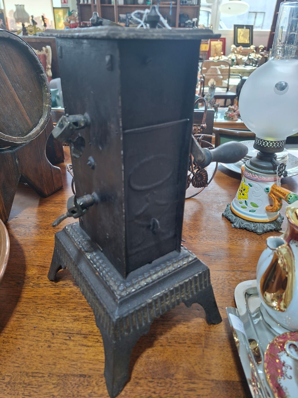 Un macinacaffè vintage in ghisa nera, appoggiato su un tavolo di legno in un negozio di antiquariato.
