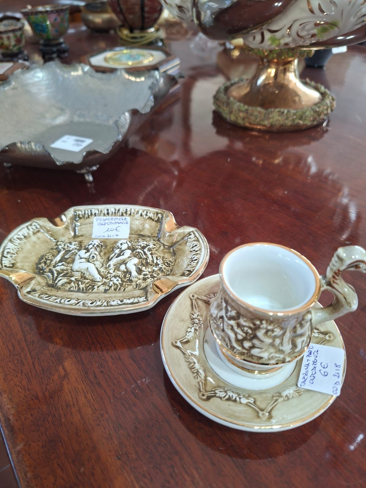 Elegante piatto vintage in ceramica color crema e oro con tazza da tè abbinata su piattino, esposto su un tavolo di legno.