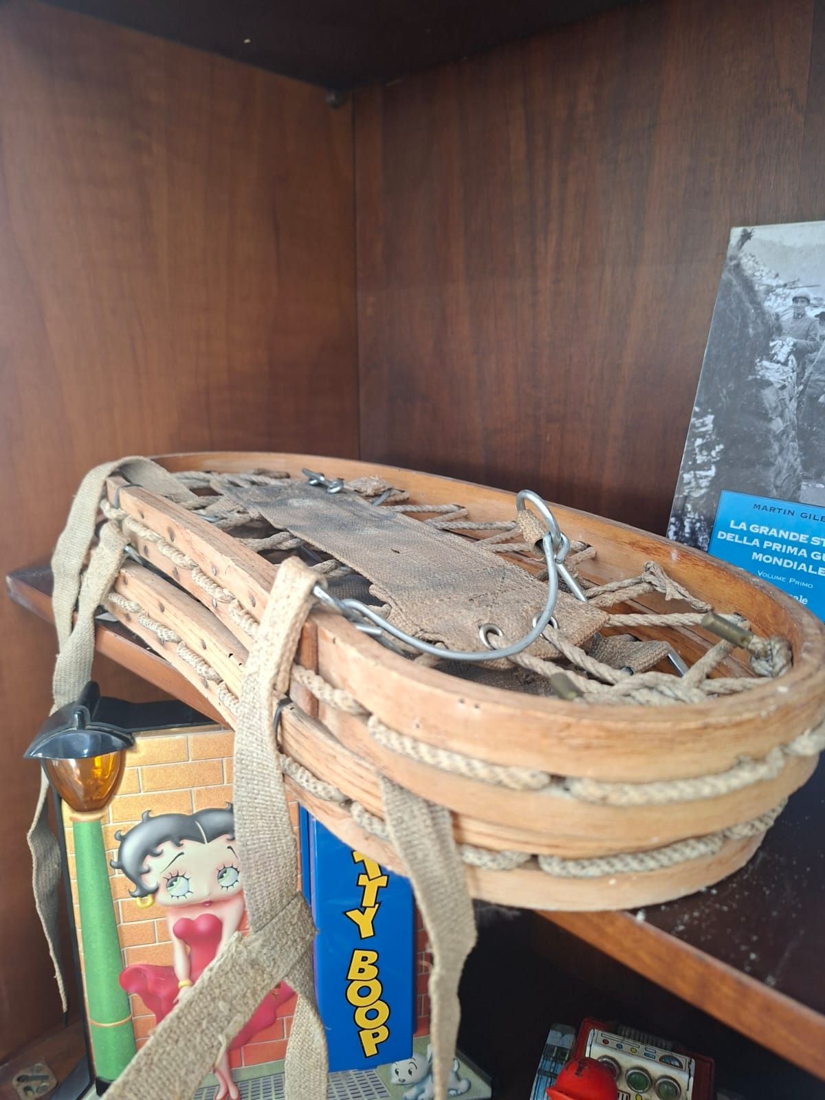 Una racchetta da neve vintage in legno con cinghie e cinghie in tela è appoggiata su uno scaffale di legno accanto a un souvenir di Betty Boop.