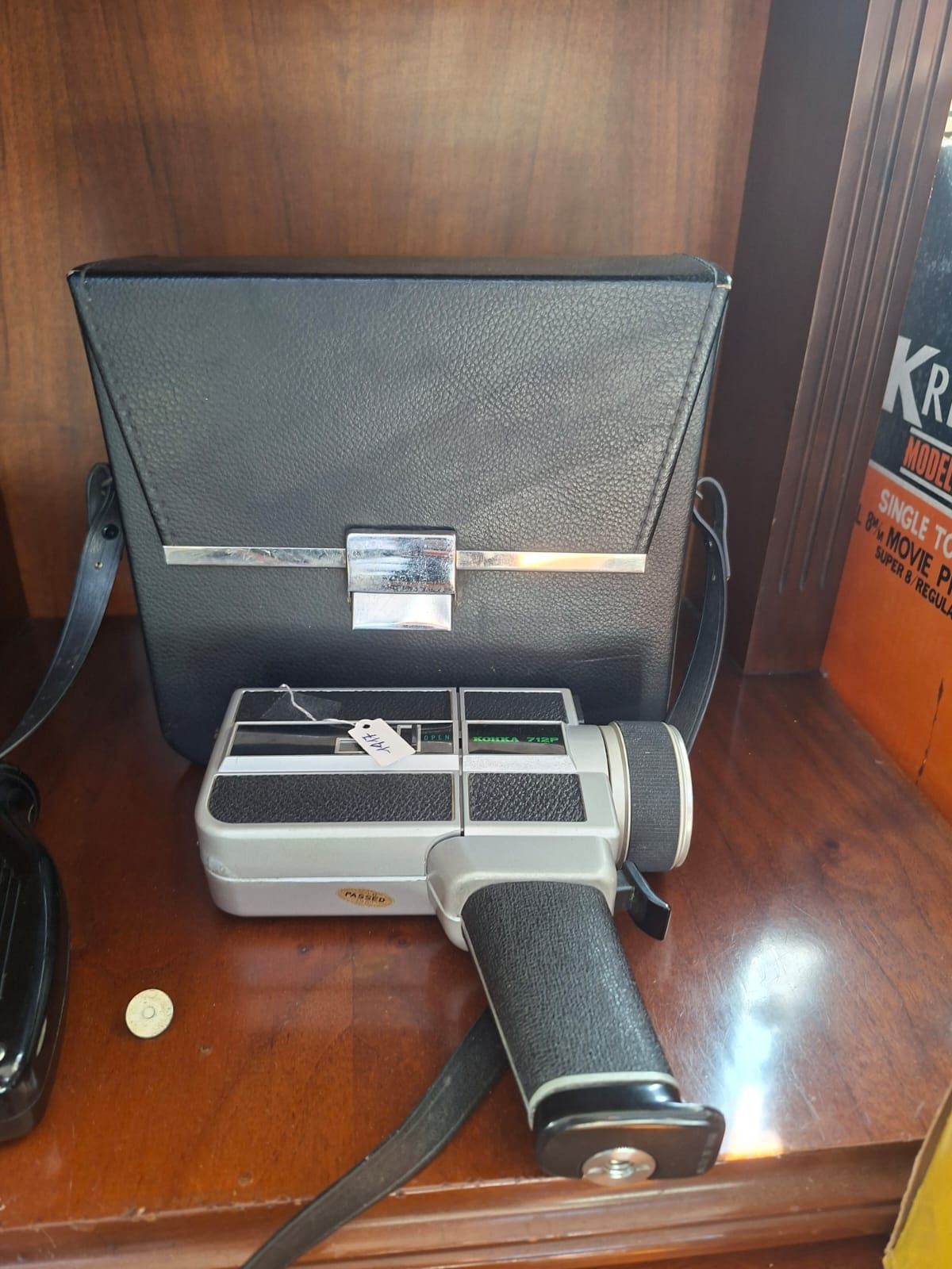 Una cinepresa vintage color argento con impugnatura a pistola nera testurizzata, appoggiata su una superficie di legno davanti alla sua custodia.