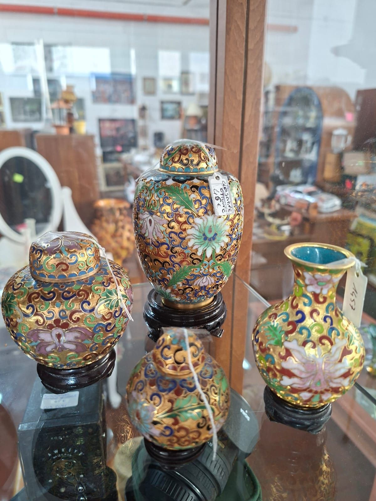 Quattro vasi cloisonné colorati e decorati, su piccoli supporti di legno, esposti all'interno di una vetrina.