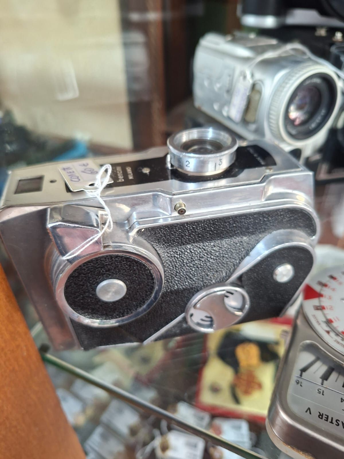 Una cinepresa vintage da 8 mm su uno scaffale, accanto a una videocamera argentata e a un esposimetro.