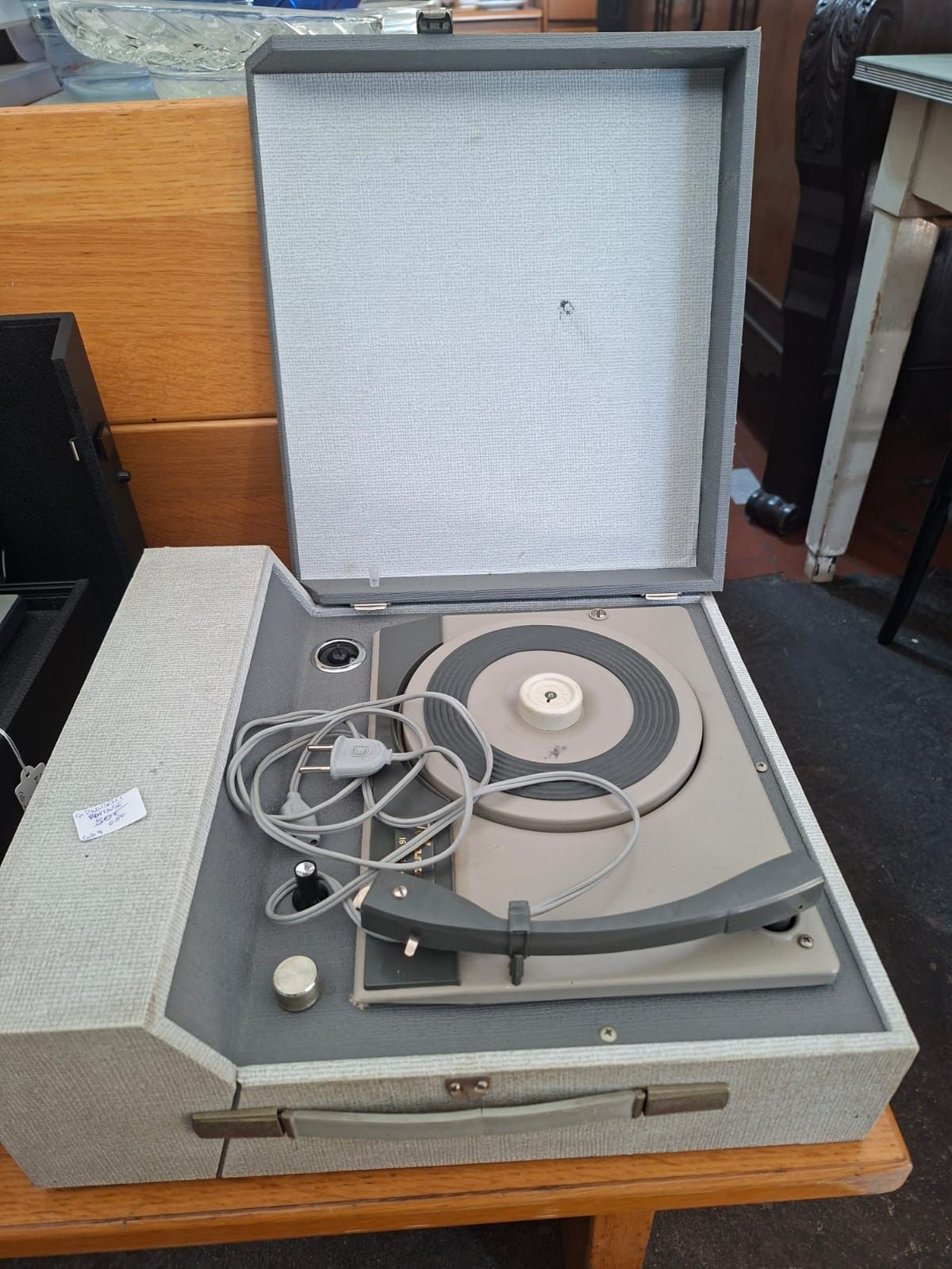 Un giradischi vintage portatile di colore grigio chiaro, con il coperchio aperto verso l'alto, appoggiato su un tavolo di legno.