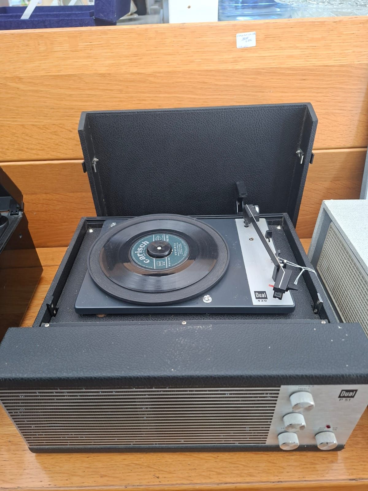 Giradischi portatile vintage nero e argento con un piccolo disco in vinile sul piatto, appoggiato su una superficie di legno.