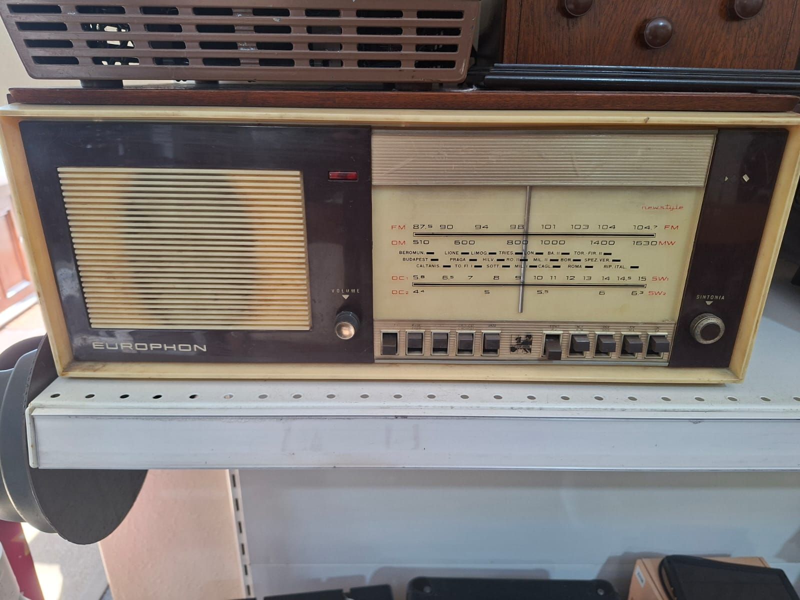 Radio da tavolo vintage beige e marrone con griglia dell'altoparlante e quadrante, posizionata su uno scaffale di un negozio.
