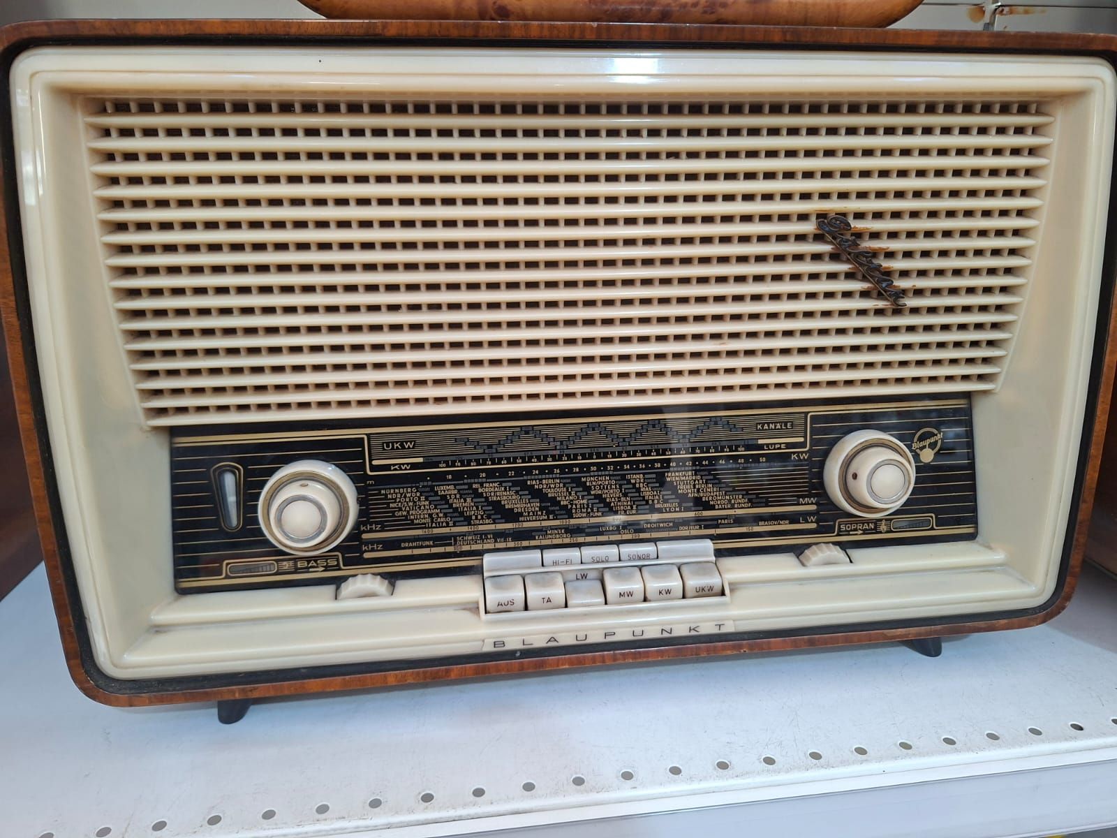 Radio da tavolo vintage in legno con griglia dell'altoparlante color crema, quadrante nero per la selezione delle stazioni e manopole di controllo.