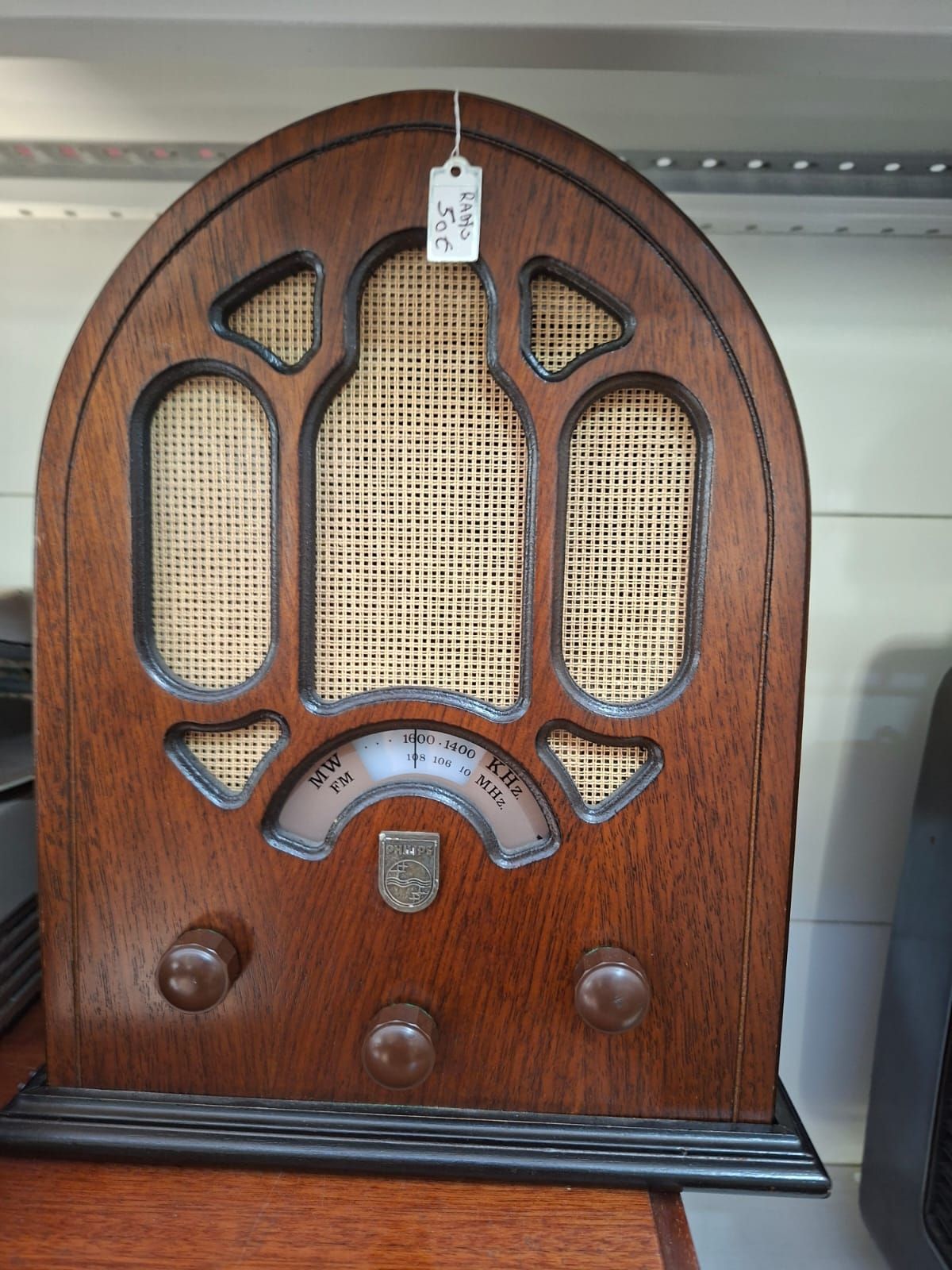 Una radio vintage in legno, in stile cattedrale, con griglie degli altoparlanti in tessuto intrecciato, tre manopole e un quadrante su una mensola.