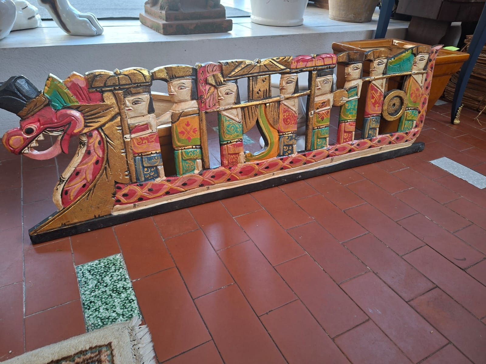 Una scultura in legno intagliata e dipinta a mano, raffigurante una barca con polena a forma di drago e figure stilizzate sedute in fila.