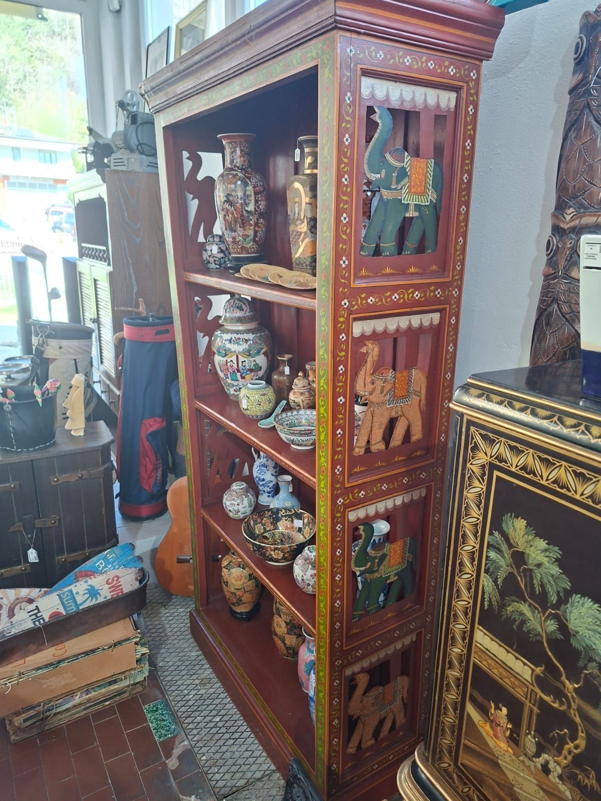 Un'alta e elaborata mensola in legno dipinta di rosso scuro e oro, con motivi di elefanti intagliati sui lati e ripiani decorativi.