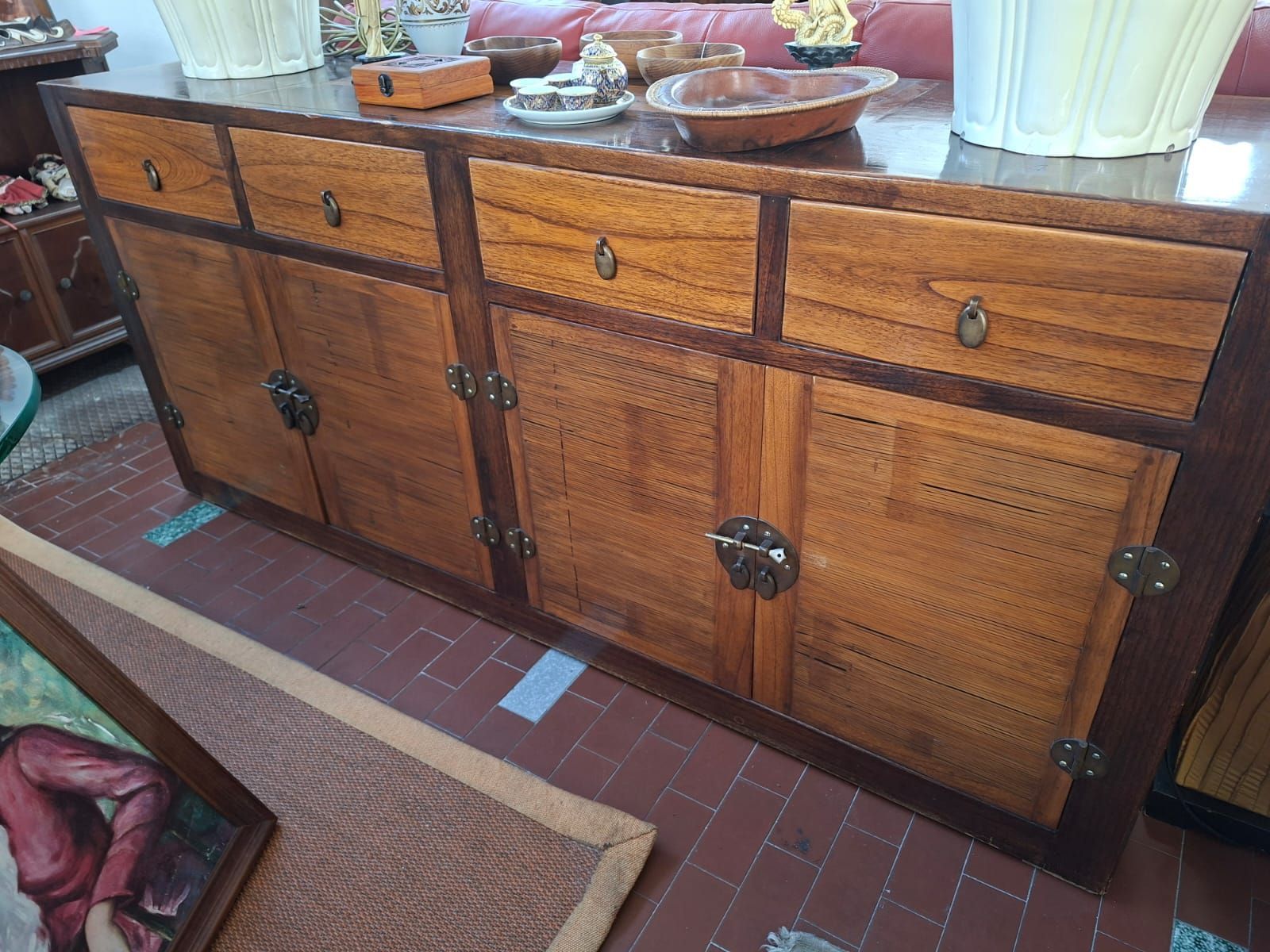 Una lunga credenza in legno con quattro cassetti sopra due coppie di ante a doppio battente, caratterizzata da pannelli che ricordano il vimini e da elementi in metallo.