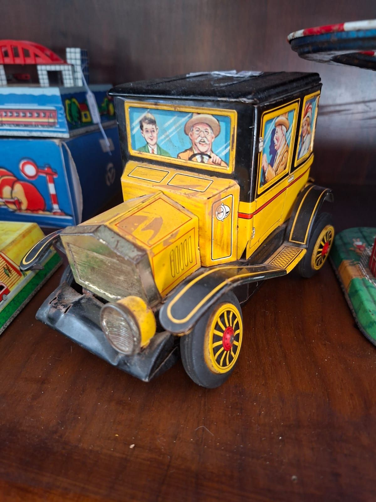Un'auto giocattolo vintage in latta gialla e nera con passeggeri illustrati seduti su una superficie di legno.