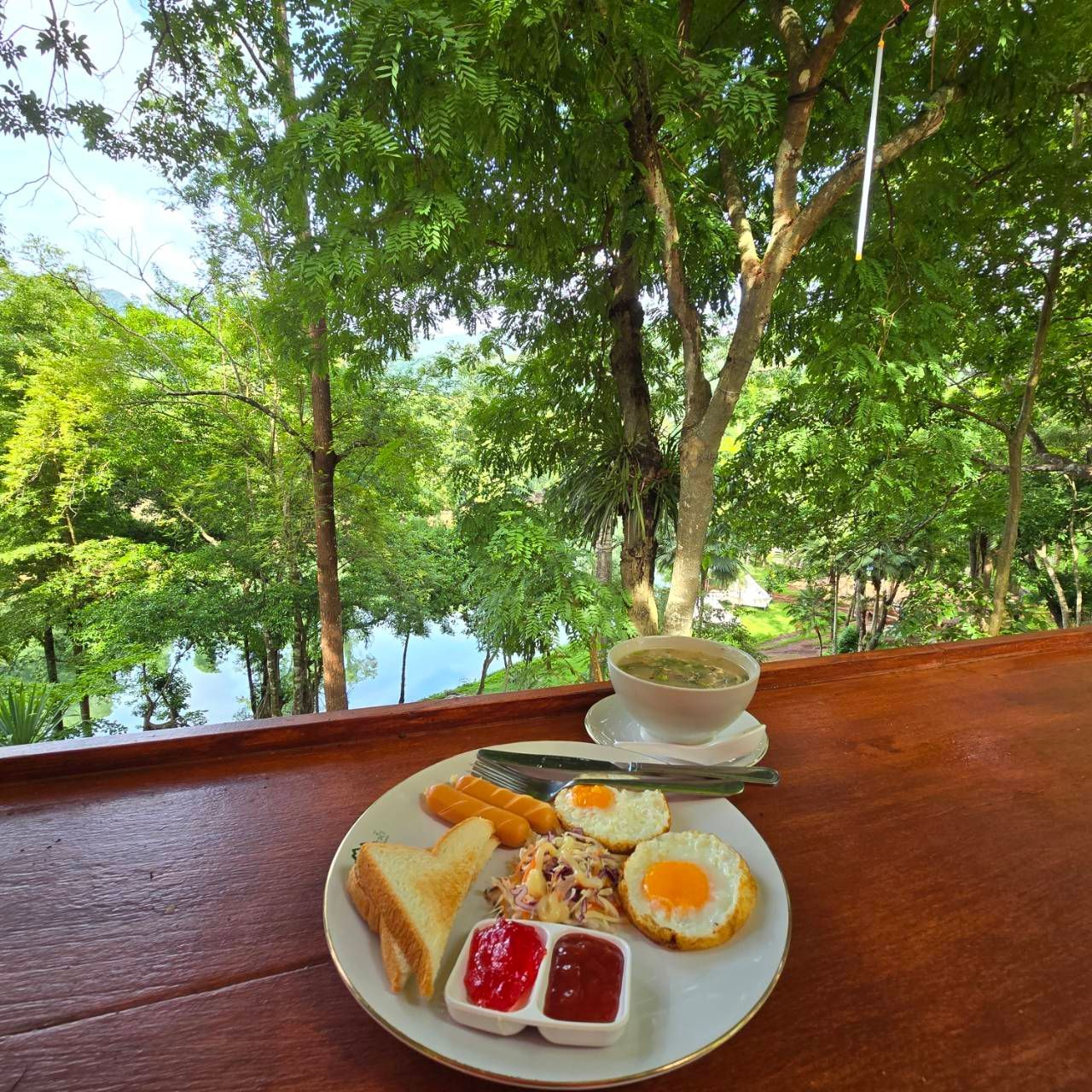 A plate of food and a cup of soup on a table with trees in the background